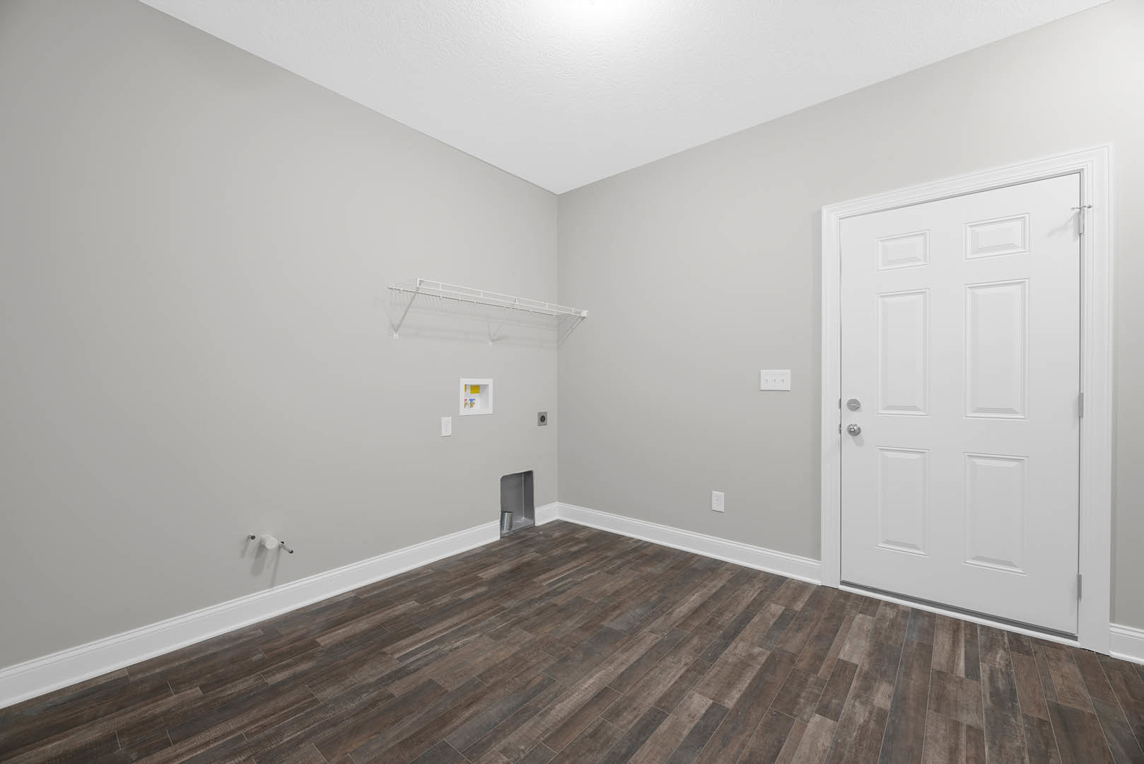 White paneled door with silver knobs, wood flooring and white baseboards, white shelving unit with a metal can on top, smooth white walls
