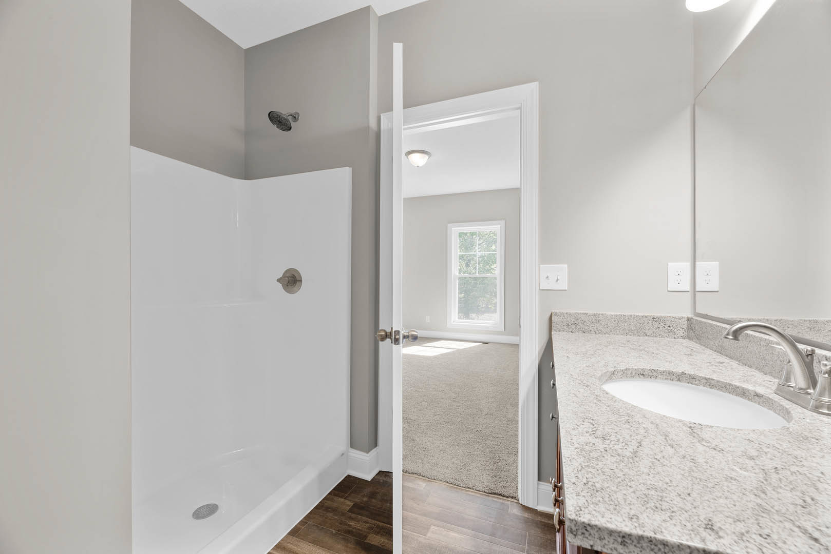 Modern bathroom featuring a tiled walk-in shower with chrome showerhead, white porcelain sink with sleek faucet, large wall mirror, and window with white frame.