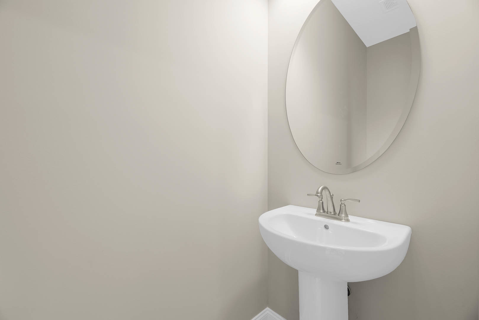 White tile bathroom featuring a round wall mirror above a white sink with a silver faucet, visible ceiling vent, and minimalistic fixtures.