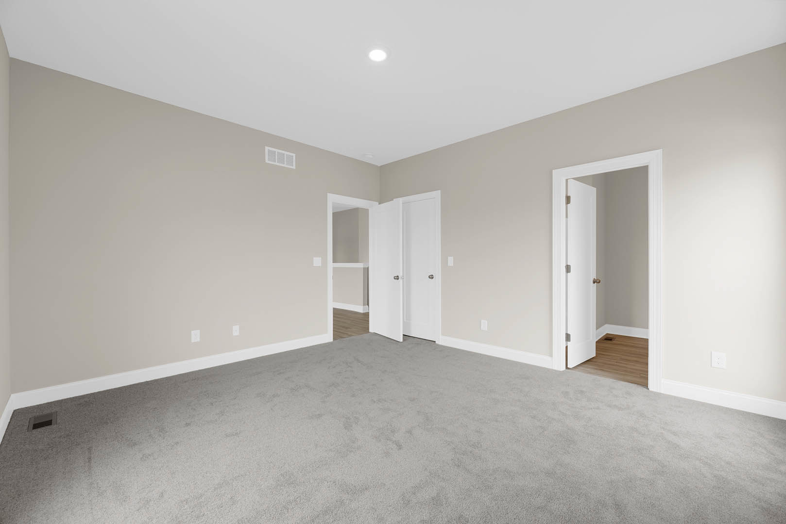 White-walled room with grey carpet flooring, open white door featuring a silver door knob, smooth plaster ceiling, and soft natural light illuminating the interior.