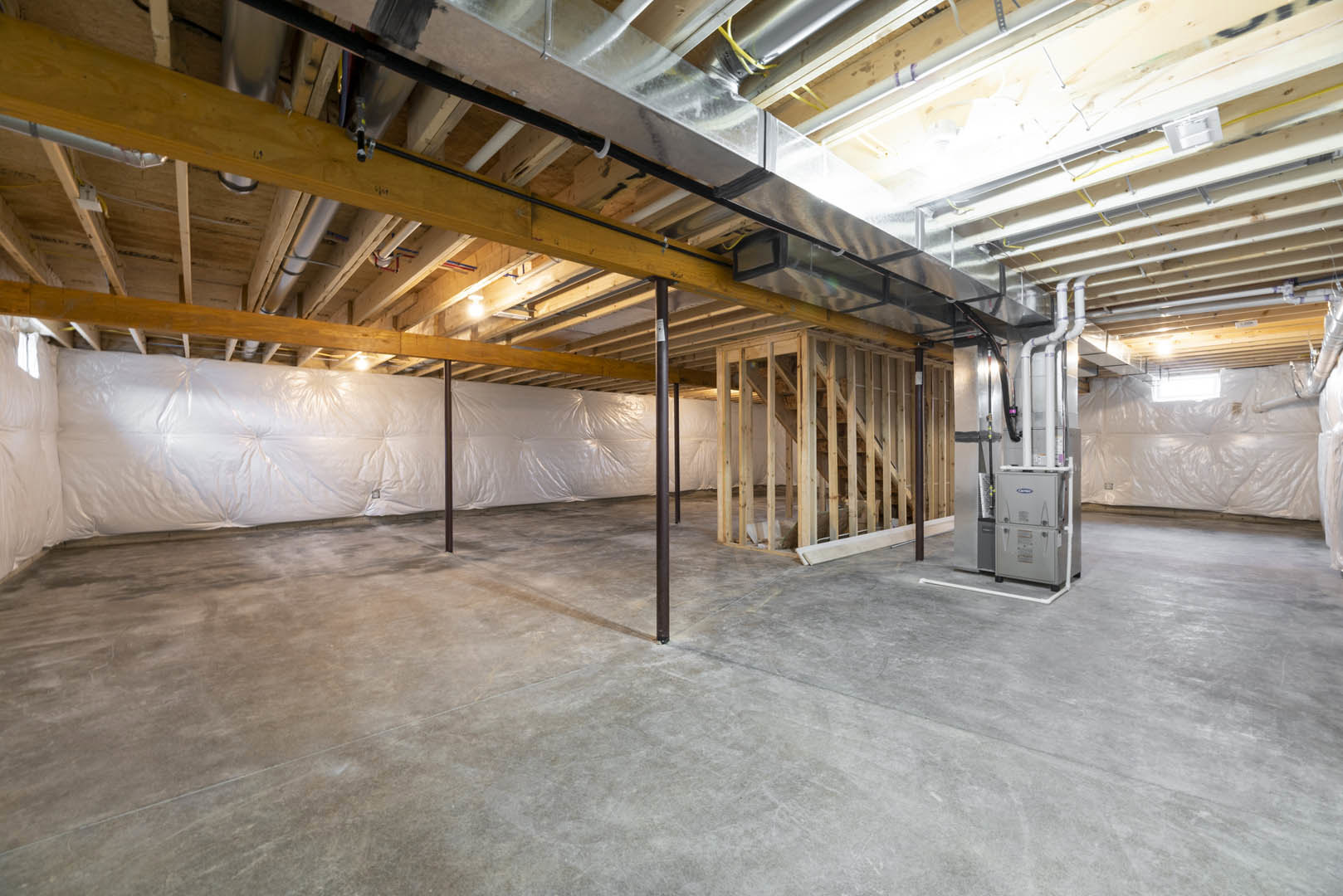 Basement room with exposed concrete floor, white walls, metal support beam, and visible heating system with metal pipes and box
