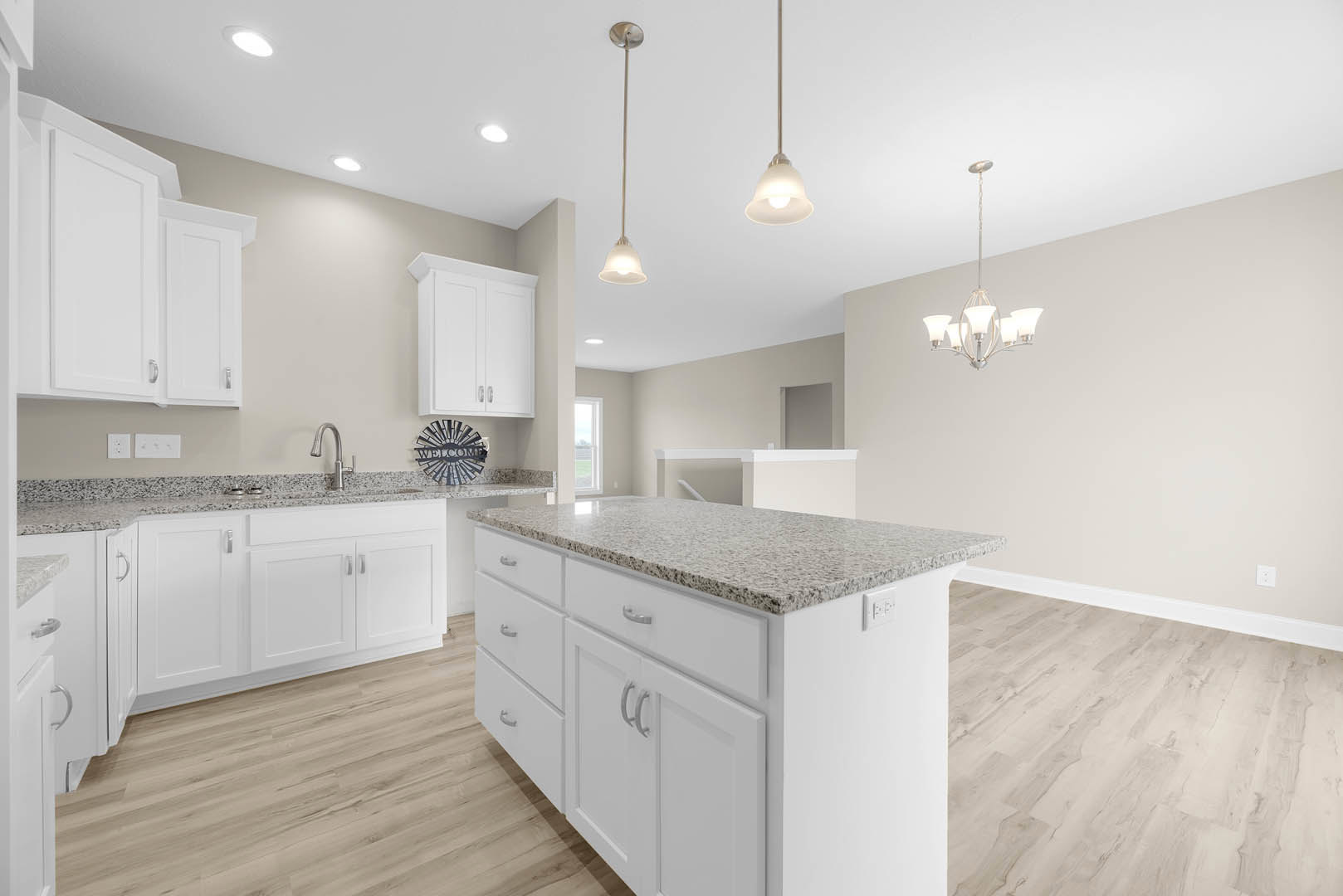 White kitchen with granite countertops, white cabinetry, kitchen island, stainless steel fixtures, tile flooring, and a decorative sunburst sign on the wall.