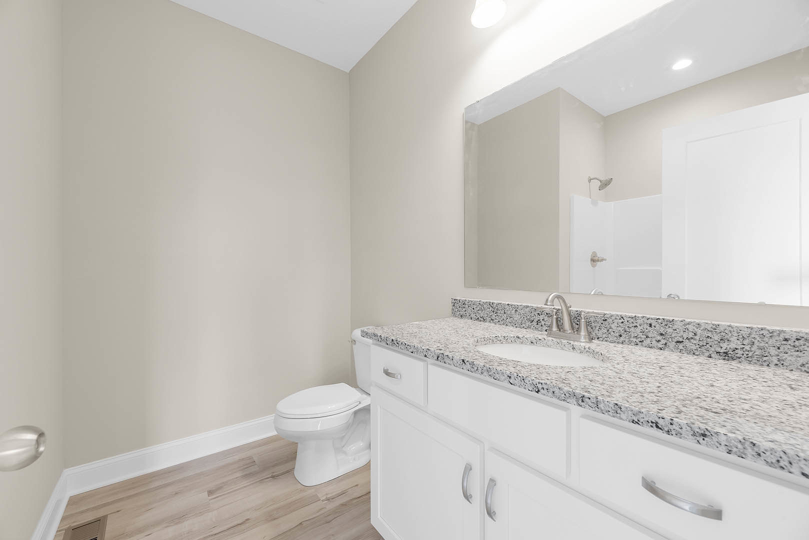 Marble bathroom countertop with undermount sink, chrome faucet, white toilet, white cabinetry, and wall-mounted light fixture