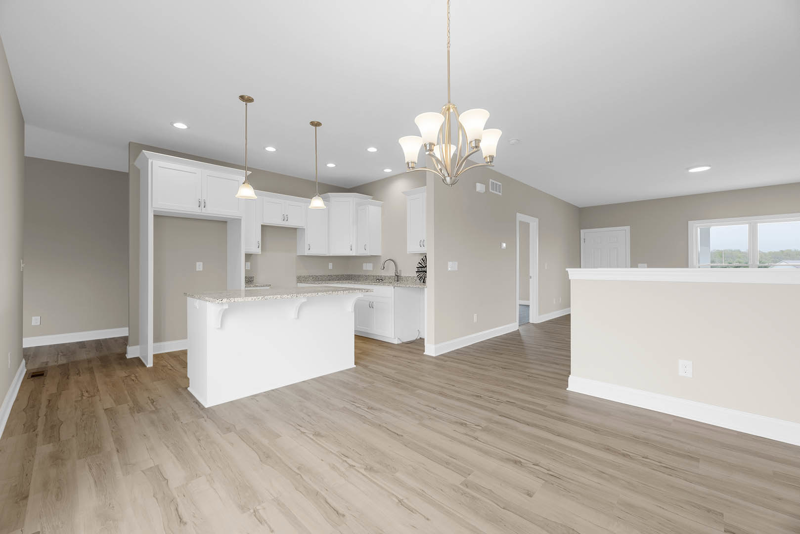 Open-concept kitchen and living room featuring a white countertop, white baseboards, hardwood flooring, large windows with views of trees, and a close-up of a chandelier hanging