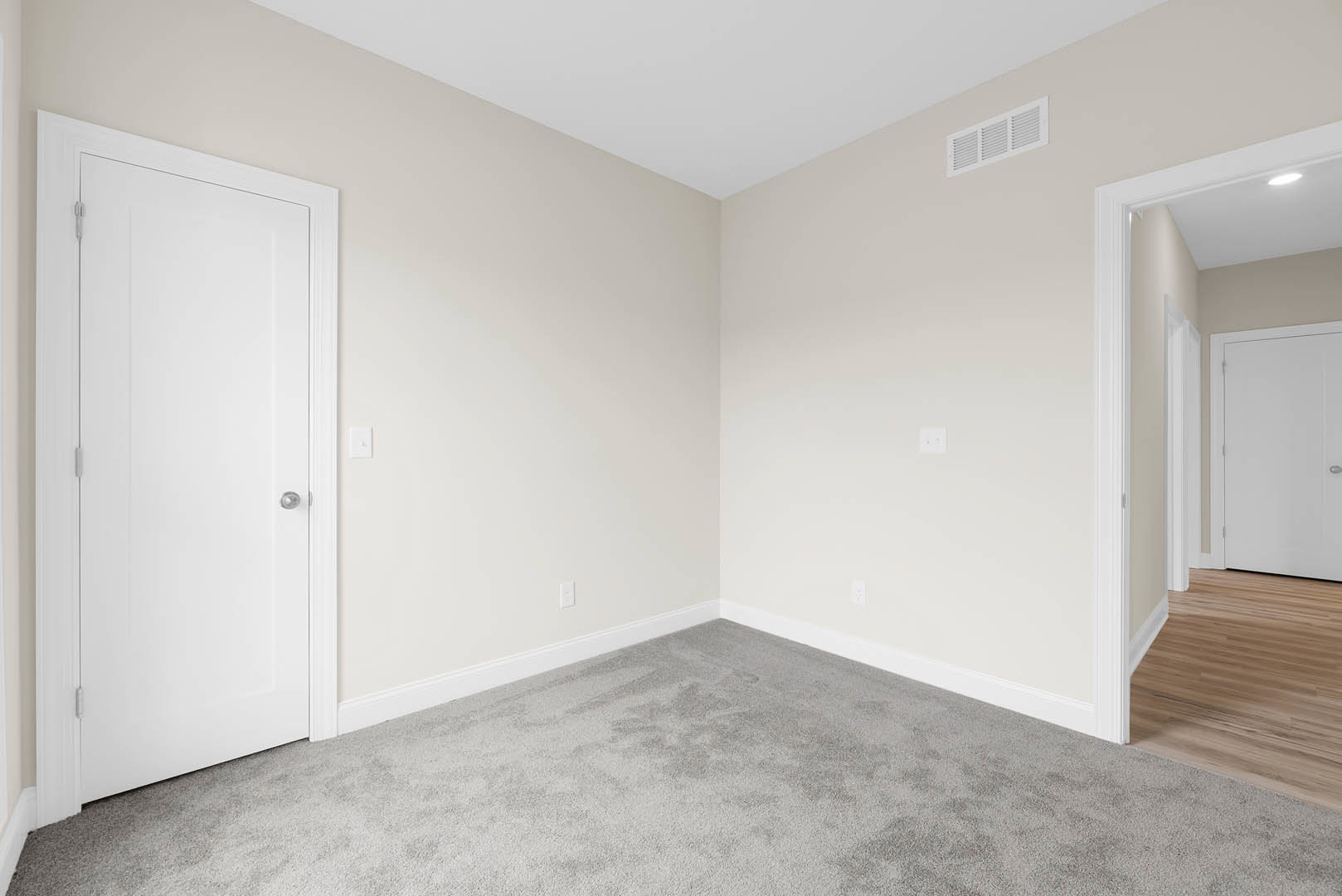 White paneled door with silver handle, beige carpet flooring, white baseboards, ceiling vent, and smooth plaster walls