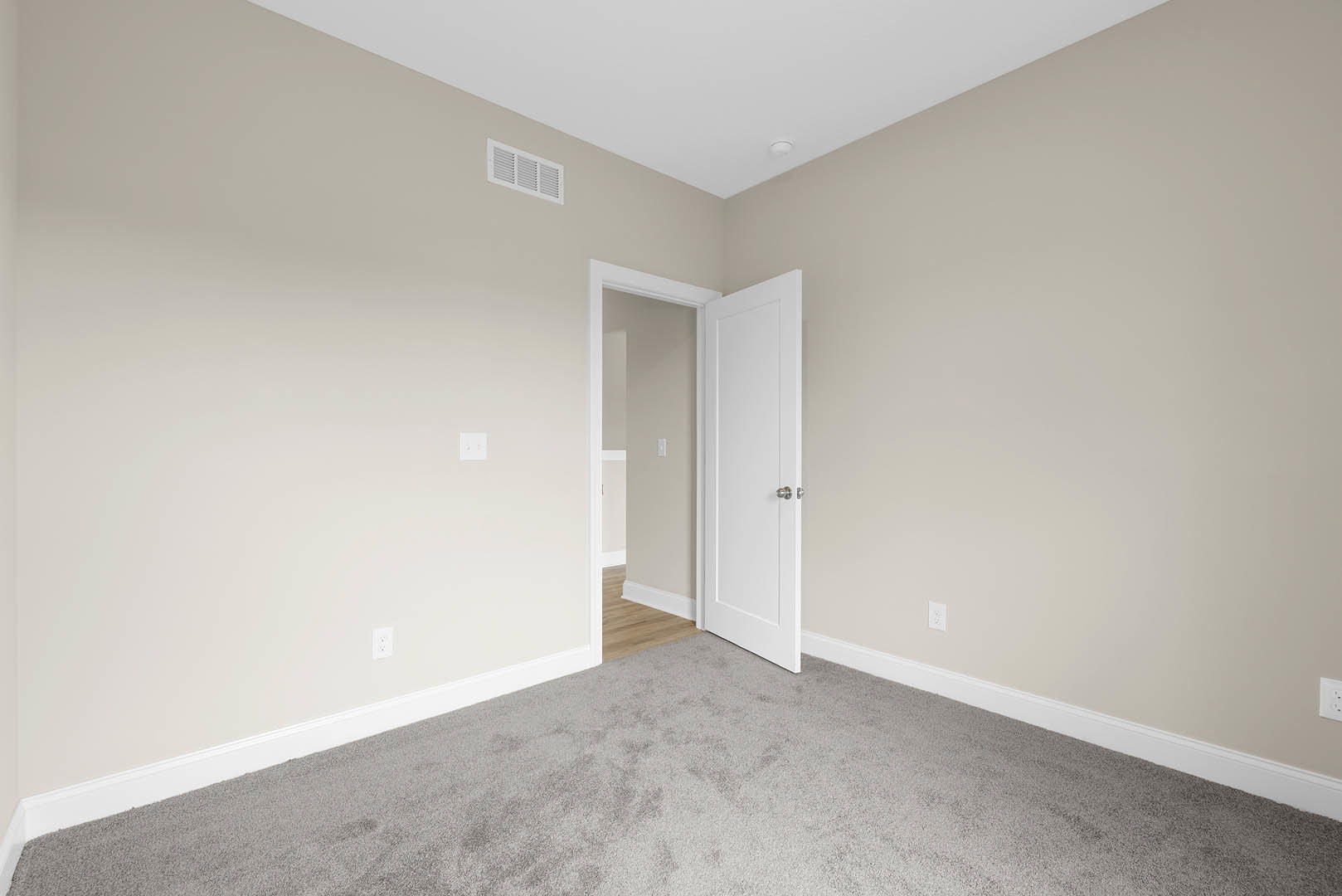 White paneled door with silver knobs open to carpeted room, wall vent and light switch visible, white ceiling with recessed light fixture