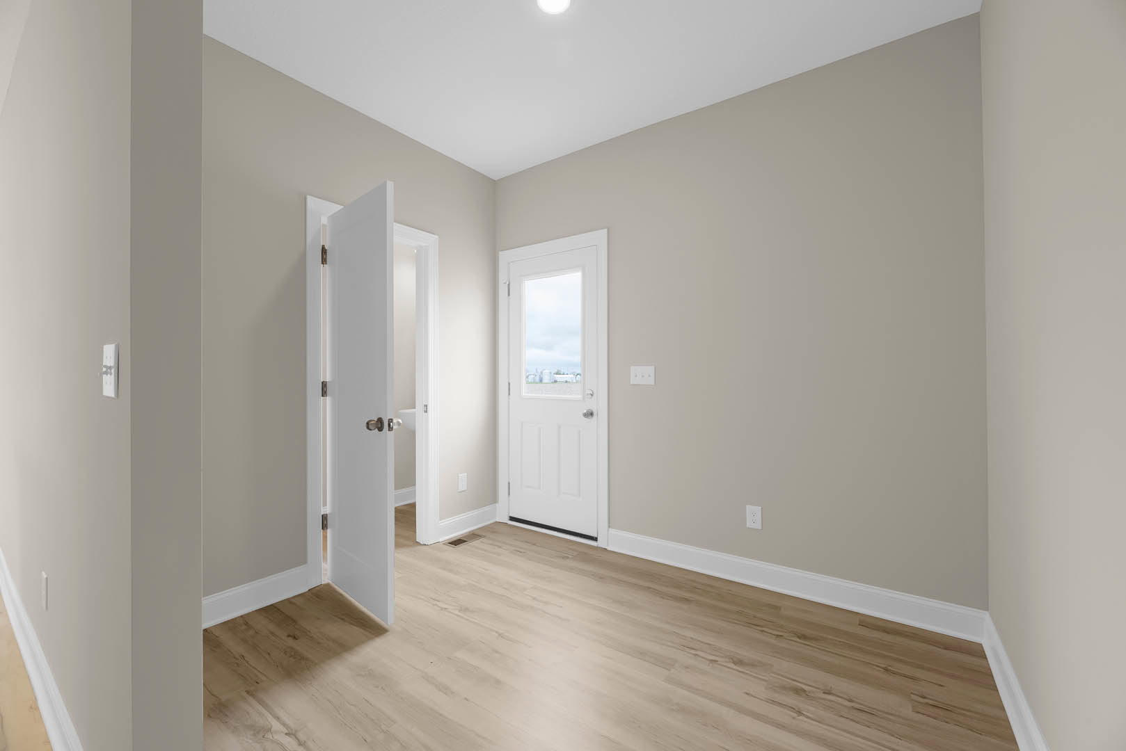 White paneled door with glass window open to a room featuring wood laminate flooring with a floor vent, white walls, and ceiling with recessed light; window offers city view.