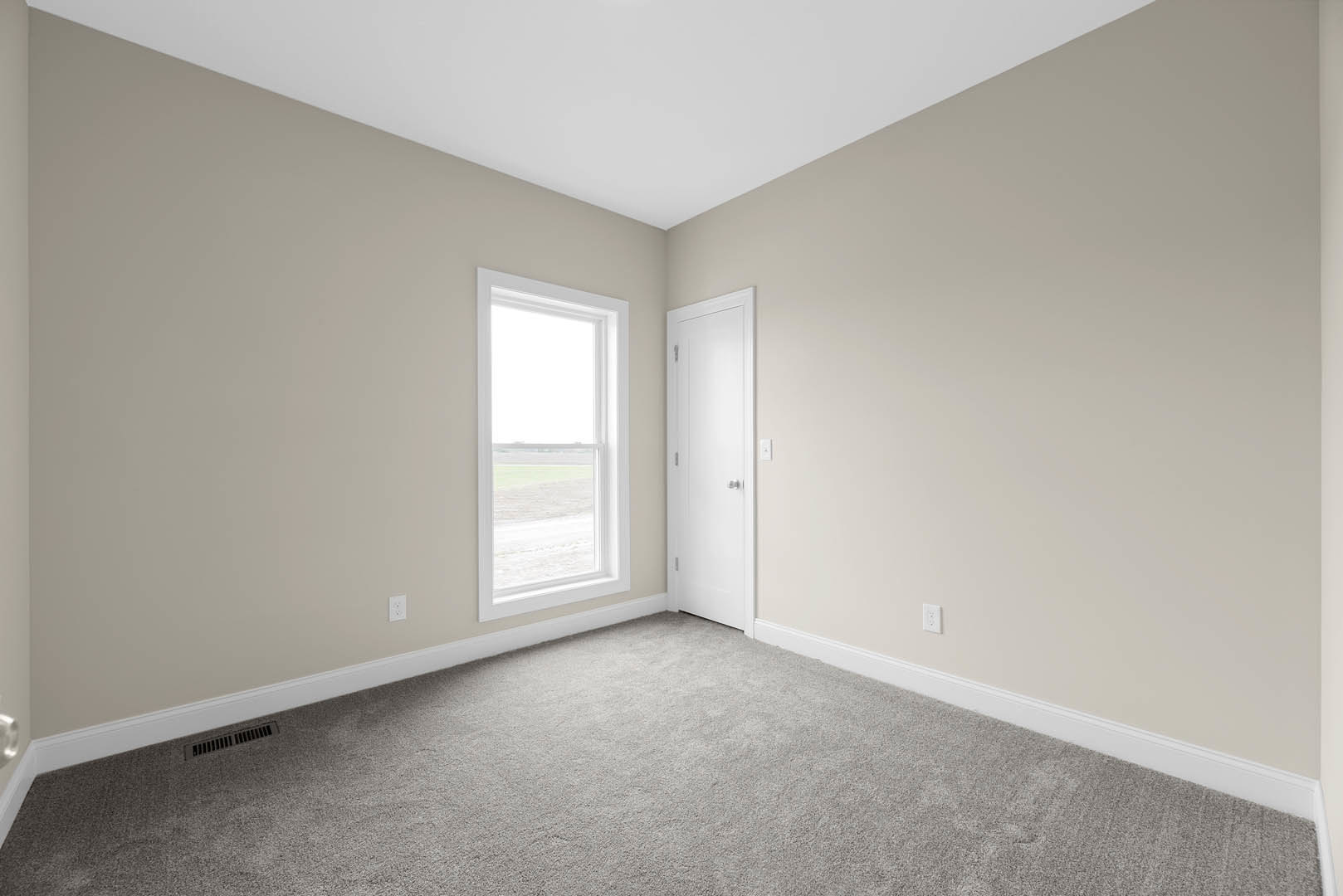 Carpeted bedroom with white walls, white ceiling, white door featuring a silver handle, large window overlooking grassy field, simple baseboard molding