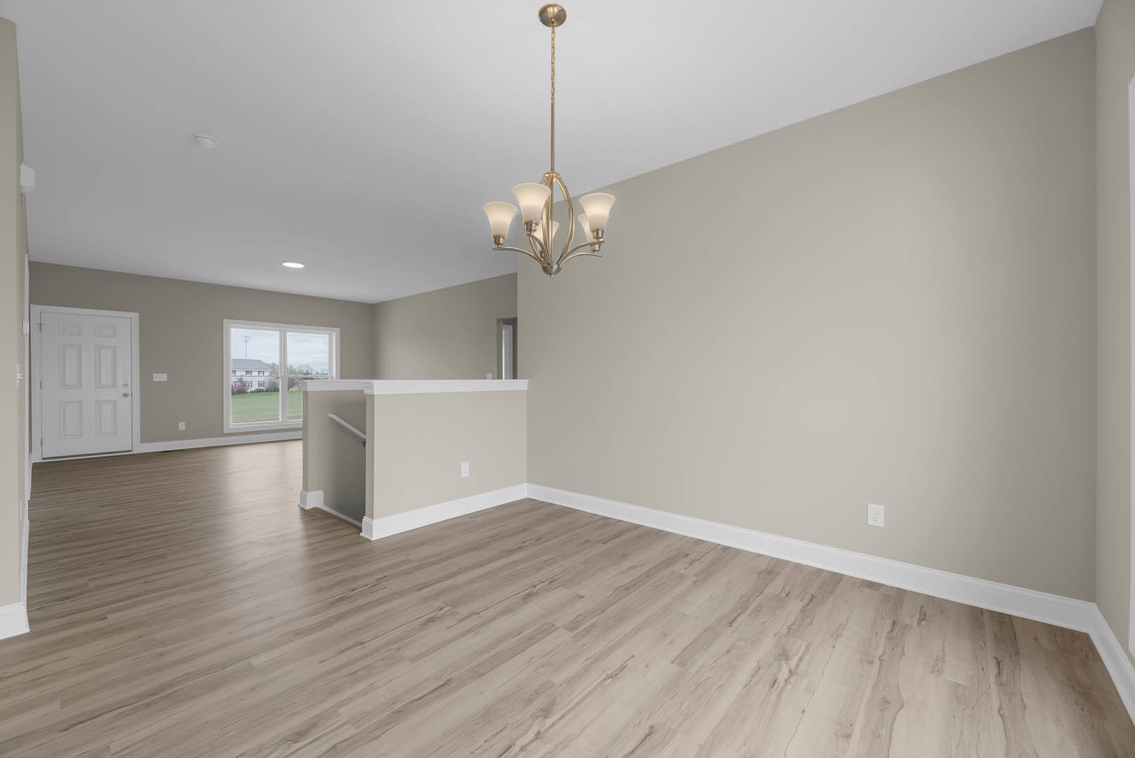 Wood flooring in a bright room with white walls and trim, silver-handled white door, large window overlooking a lawn and neighboring house, and a modern chandelier hanging from the