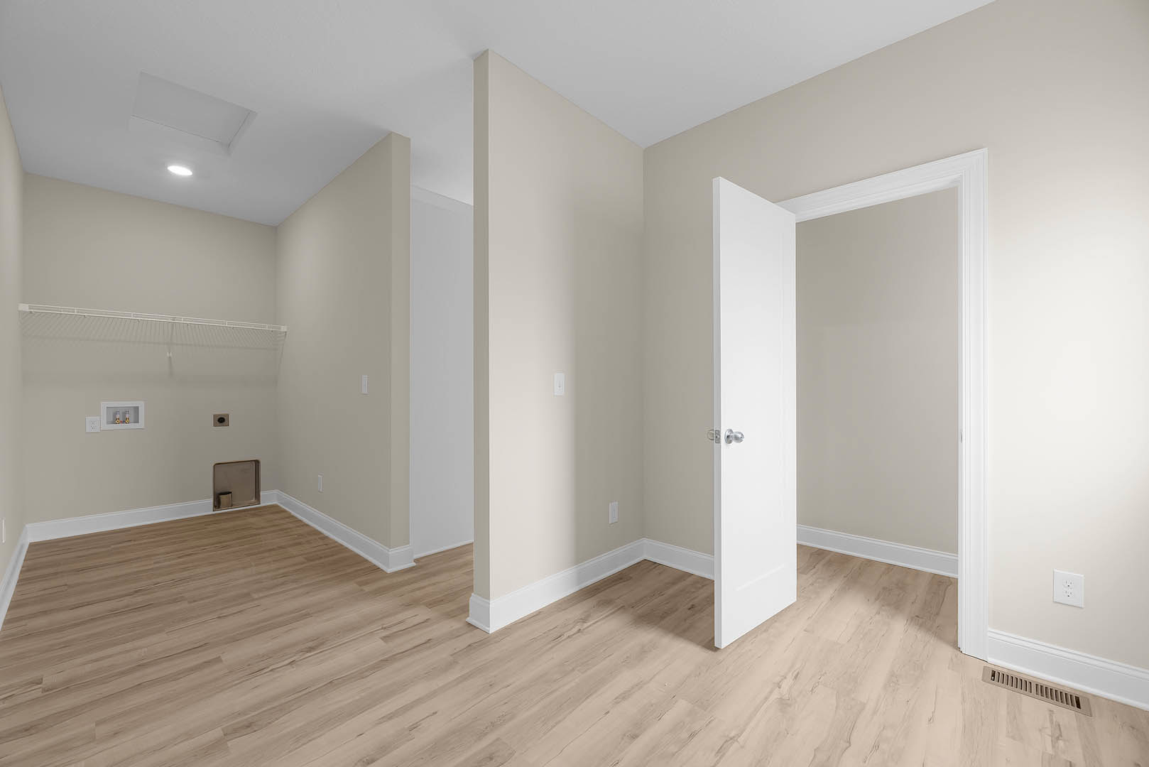 Wood floor with white baseboards, white door with silver knob open to adjoining space, white outlet and small metal container on white plaster wall, white railing visible along