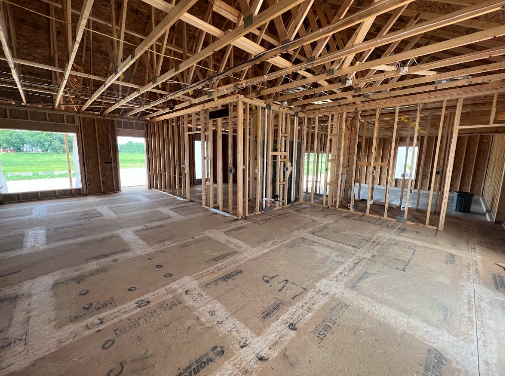 Exposed wood ceiling beams, large window with natural light, unfinished walls, construction materials visible