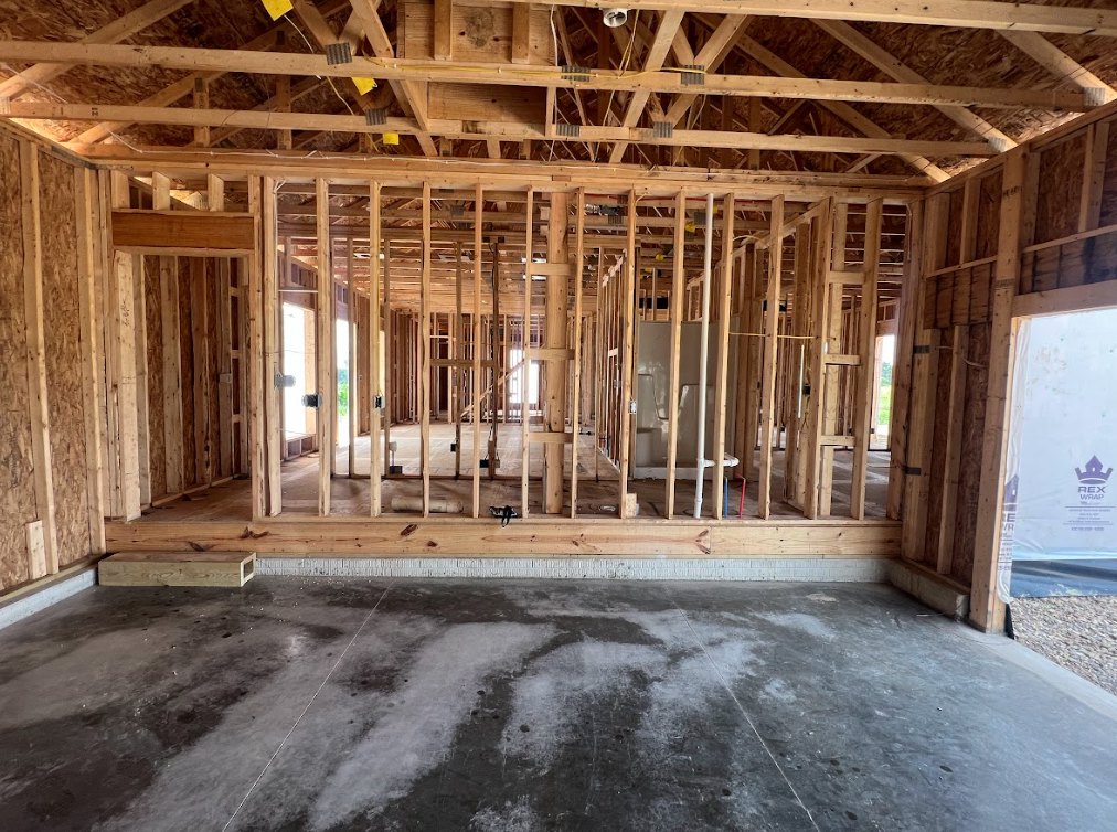 Exposed wood framing with ceiling beams, visible floor planks, and a light fixture; construction materials and insulation in a partially finished interior room.