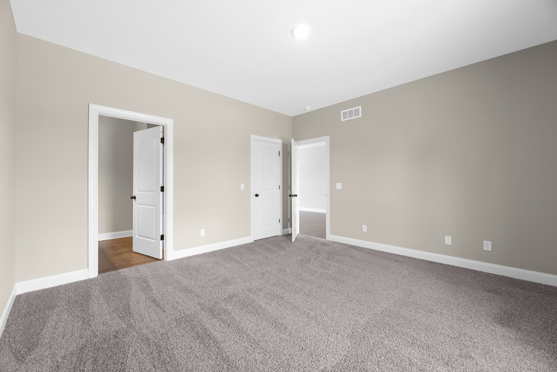 Carpeted room with white paneled doors featuring black knobs, white walls, and smooth ceiling