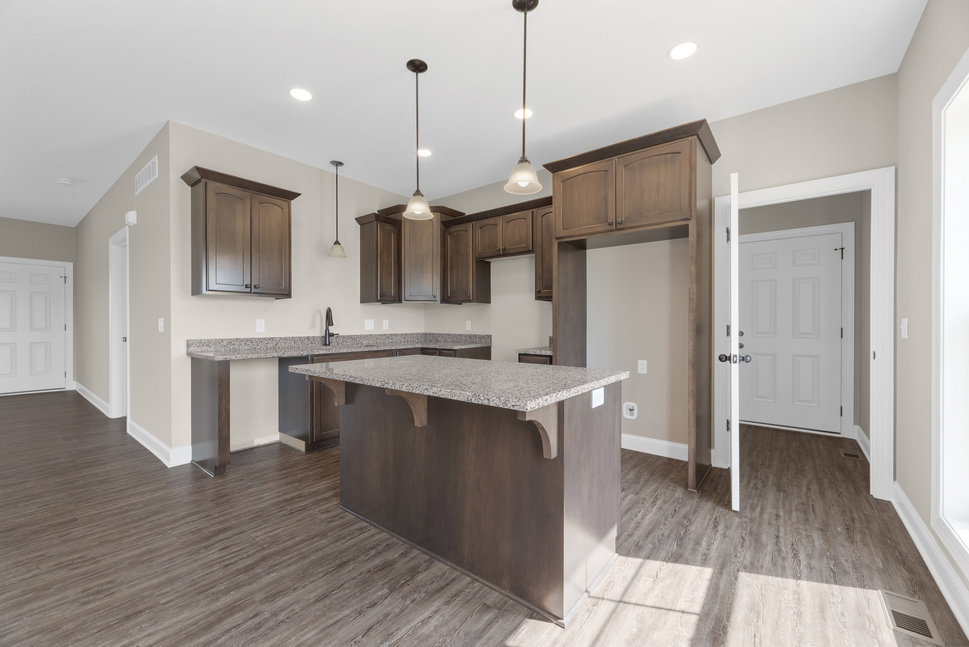Open kitchen with granite countertops, wood flooring, bar seating, white paneled door with silver knobs, modern ceiling light fixture, and light-colored cabinetry.