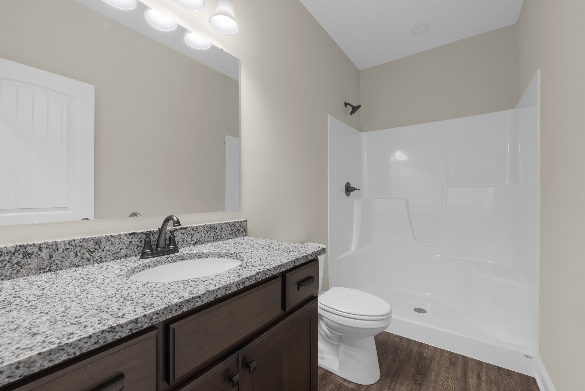 Bathroom with wood flooring, white toilet, white sink set in a dark cabinet, chrome faucet, glass shower enclosure, white door with matching trim, light-colored wall tile.