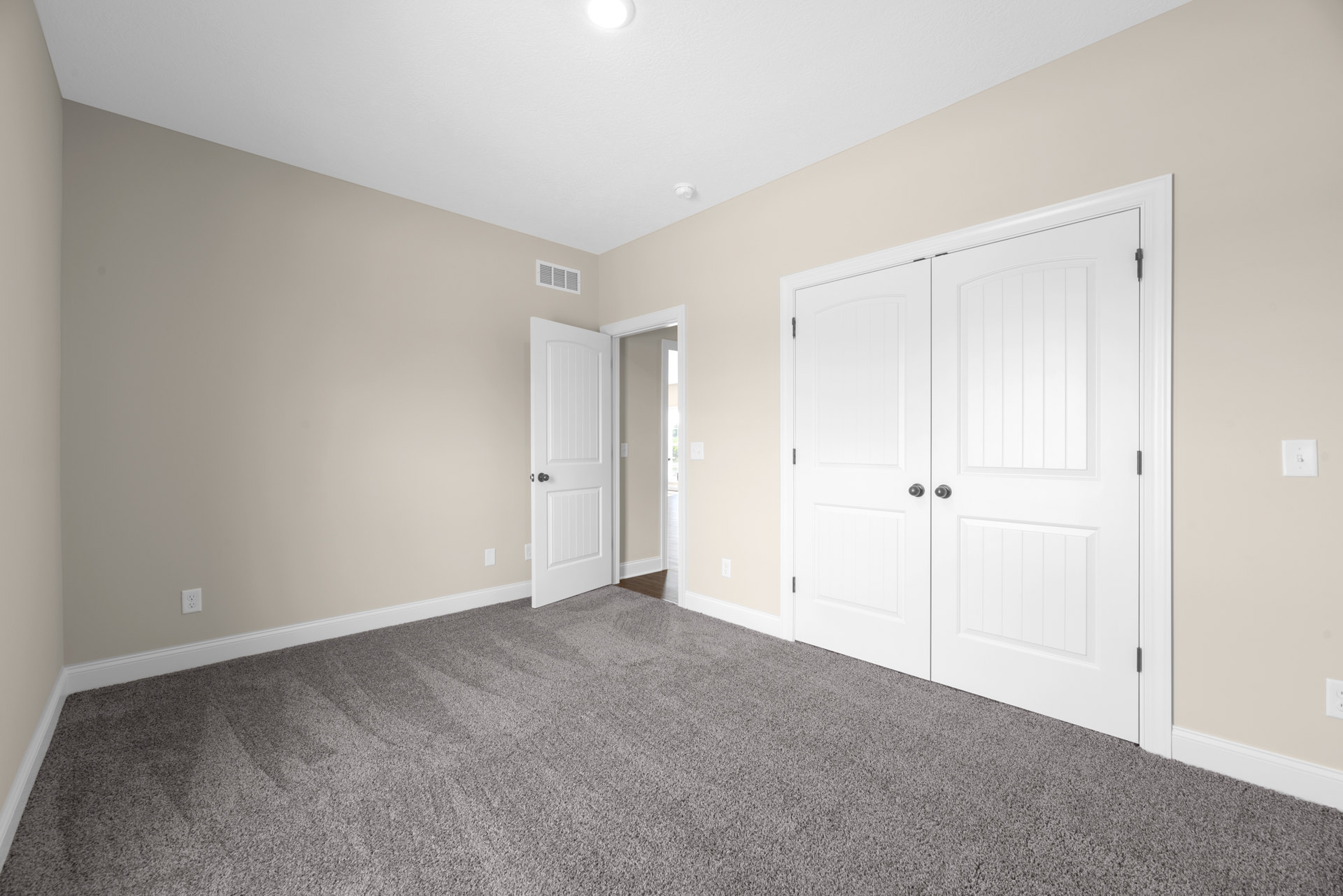 White double doors with black knobs set in a carpeted room, light switch on adjacent wall, smooth white walls and ceiling