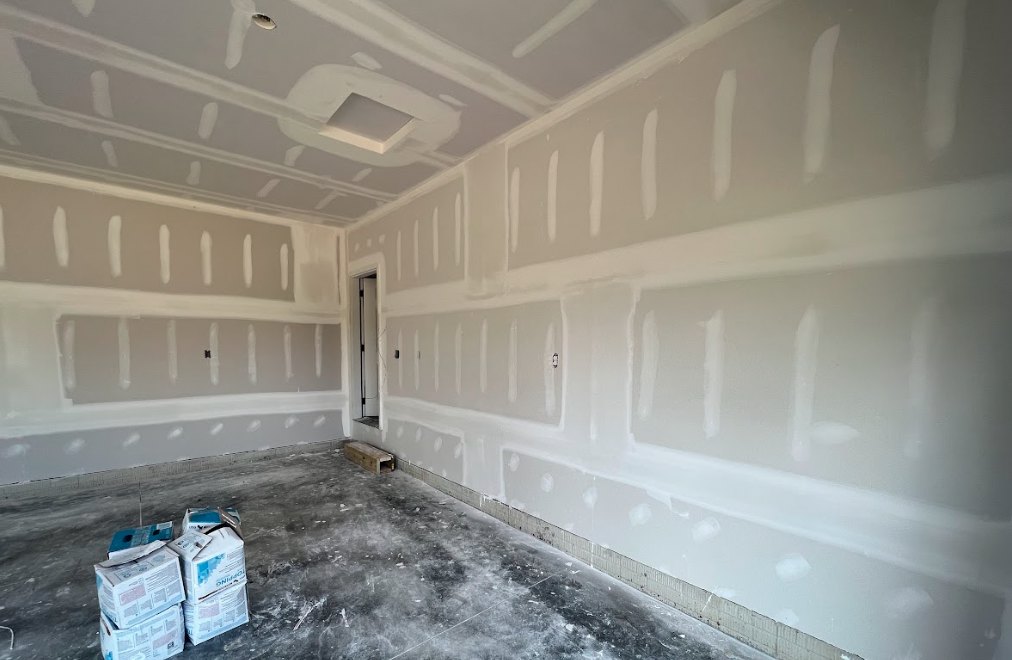 White-walled room with white painted ceiling, closed door, and stack of cardboard boxes on the floor and table