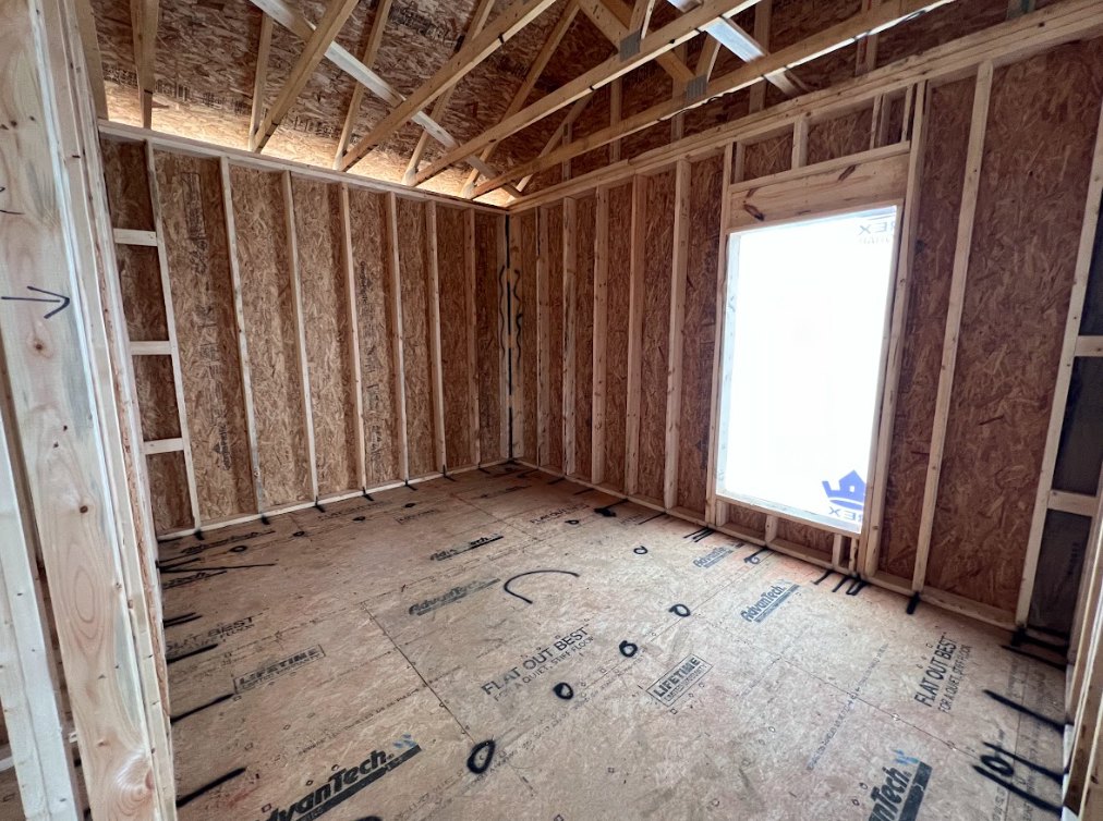 Sunlit room featuring wide wood plank flooring, exposed wooden ceiling beams, and a large window framed by white walls