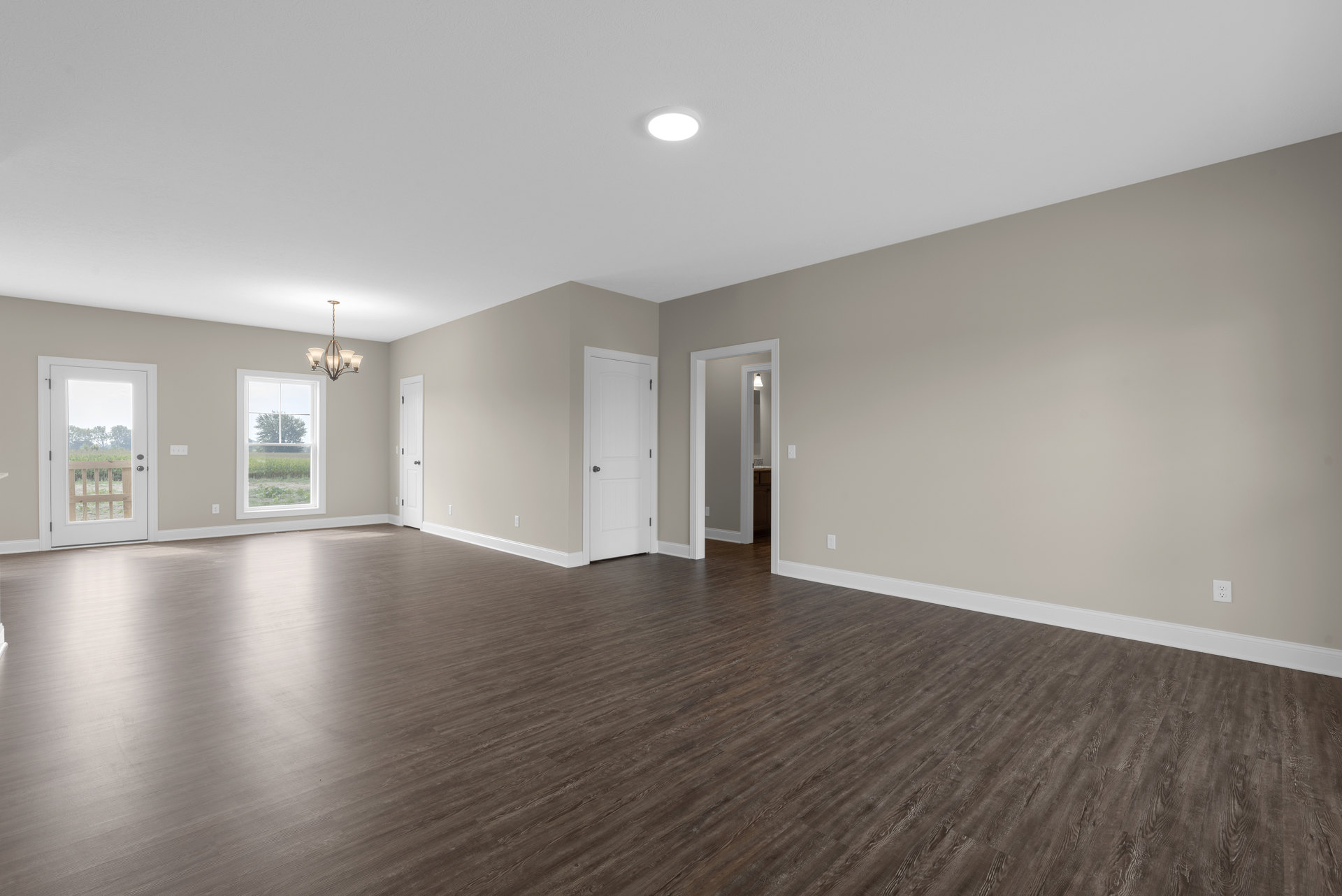 Wood flooring and white walls in a bright room, black door knob on a white door, ceiling chandelier, window and door with views of trees and a wooden fence outside