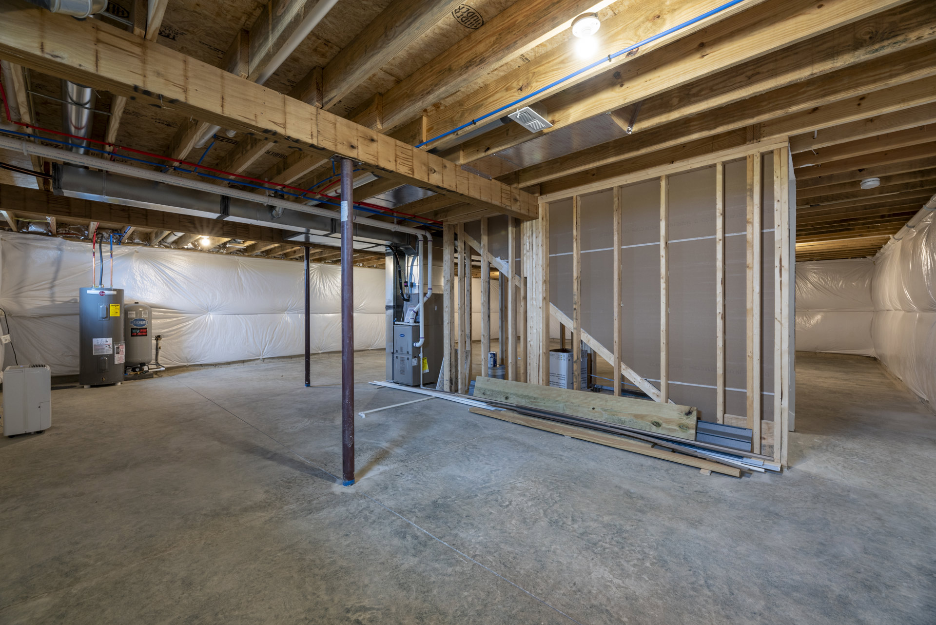 Open room with exposed wood ceiling beams and a central metal beam, white rectangular cabinet with handle, light fixture mounted on wood surface, neutral walls and flooring.