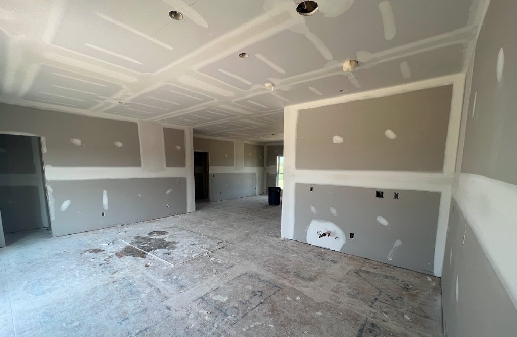 Room with smooth white plaster walls, concrete floor showing dirt, white ceiling, window close-up, exposed pipe on wall, white object with black handle