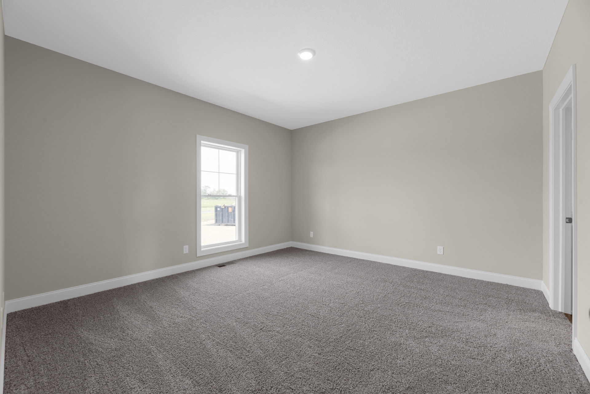 Carpeted room with white walls, large window overlooking outdoor bin, ceiling light fixture, and white door with molding