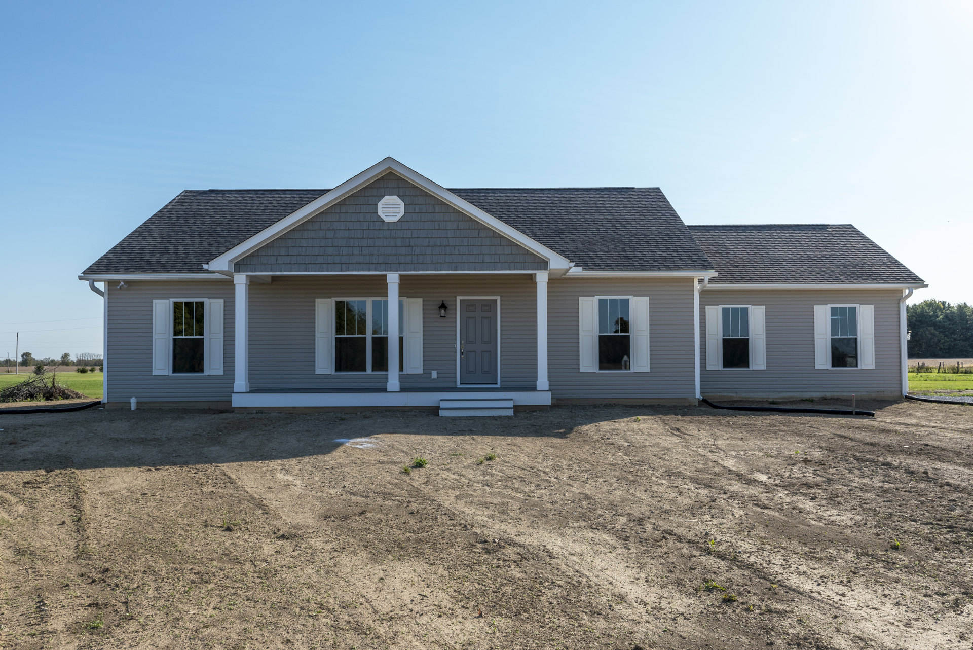 Gray house with white trim, covered porch, gray front door, shuttered window, and bare dirt yard in front.