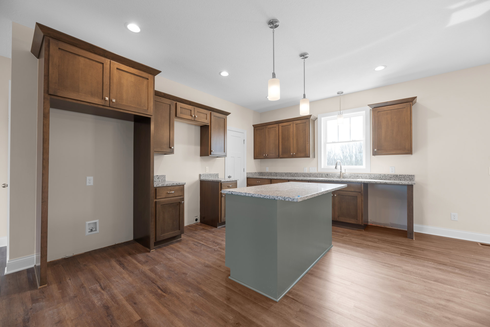 Open kitchen with central island featuring granite countertops, white cabinetry with black hardware, wooden upper cabinets, tile flooring, stainless steel sink beneath a window
