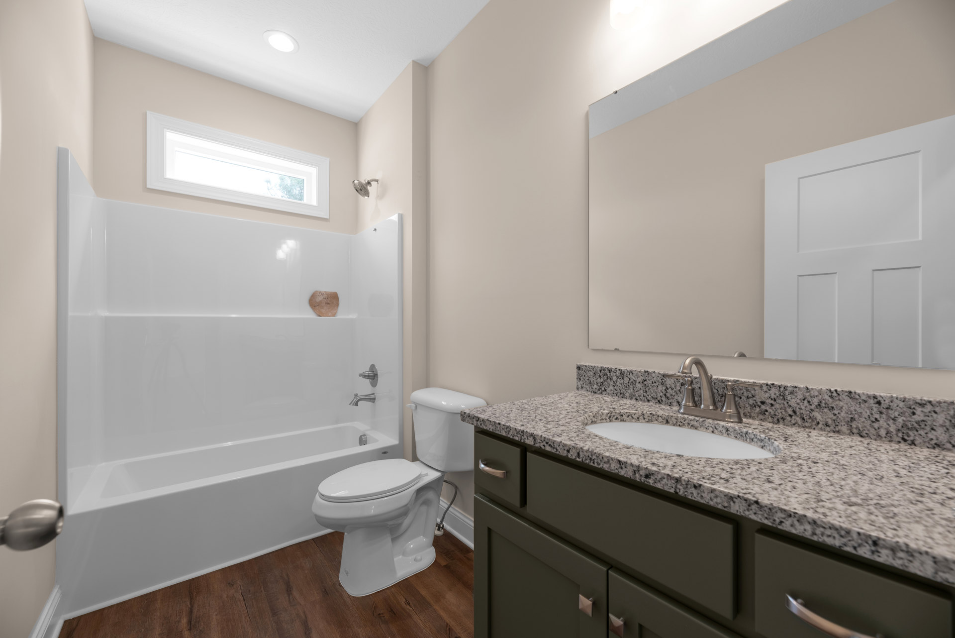 Bathroom with white bathtub, toilet, and sink set in light tile, wood cabinetry beneath countertop, square panel door, chrome fixtures, and neutral wall finishes.