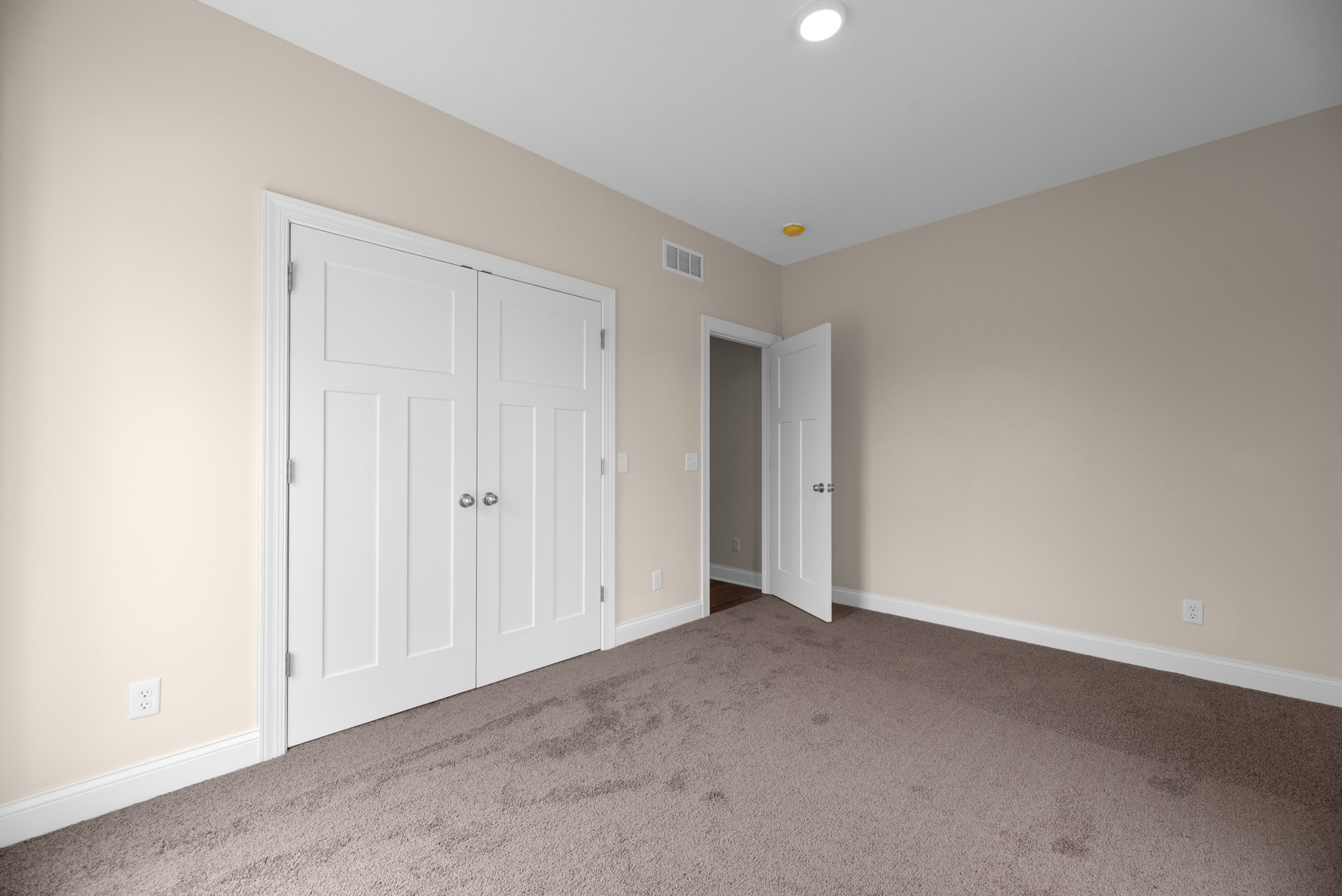White carpeted room featuring white paneled doors with silver knobs, white closet doors, smooth plaster walls, ceiling light fixture, and crown molding.