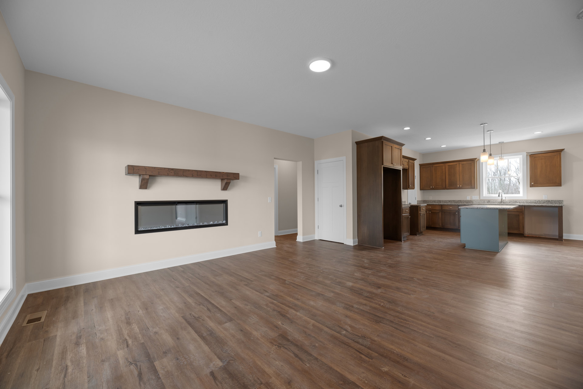 Spacious room with natural hardwood floors, open kitchen featuring white cabinetry, stainless appliances, and modern ceiling lighting; black-framed fireplace with glass and crystal