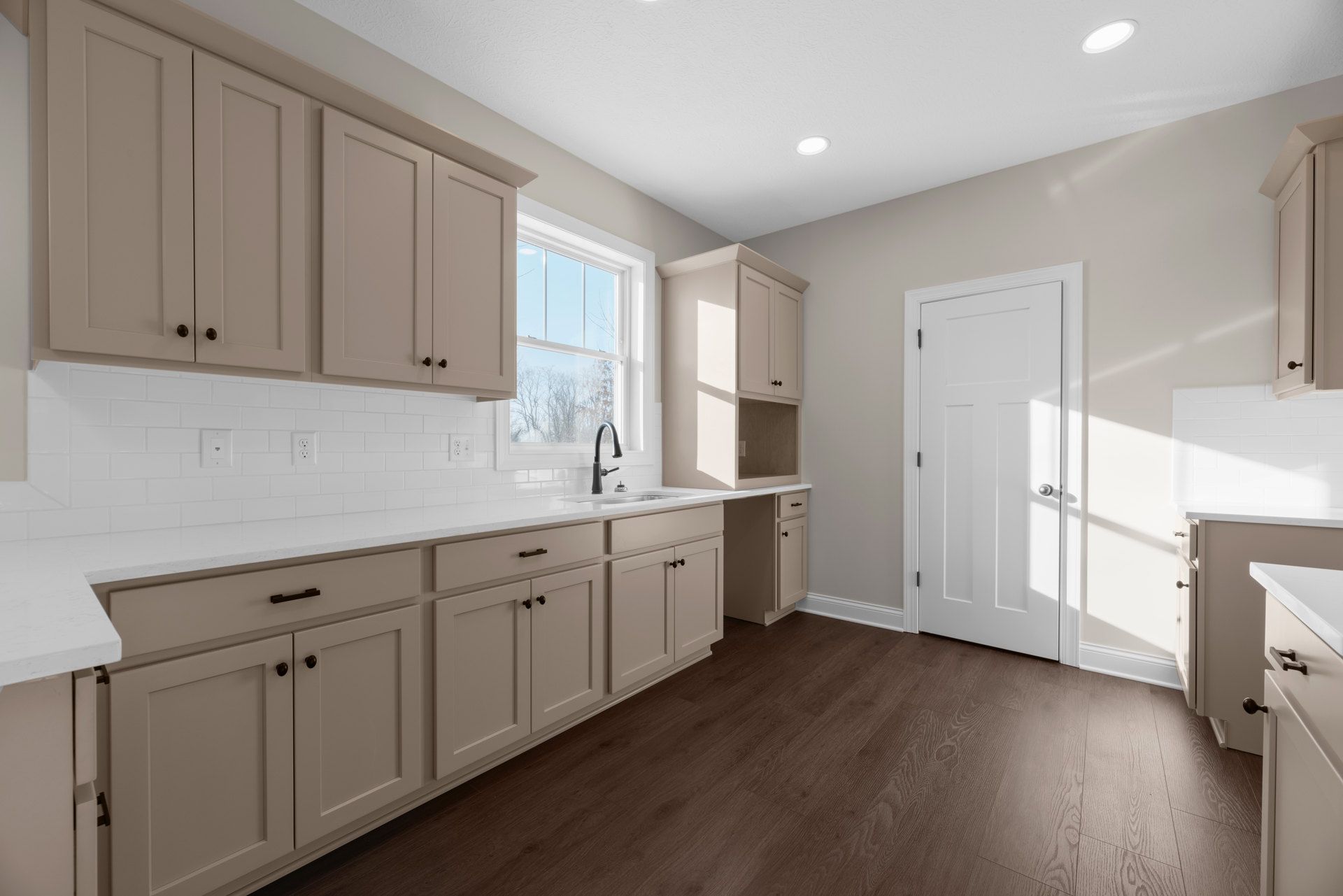 White kitchen with shaker cabinets, stainless sink, stone countertop, ceiling light, white door with silver handle, and window above the counter.