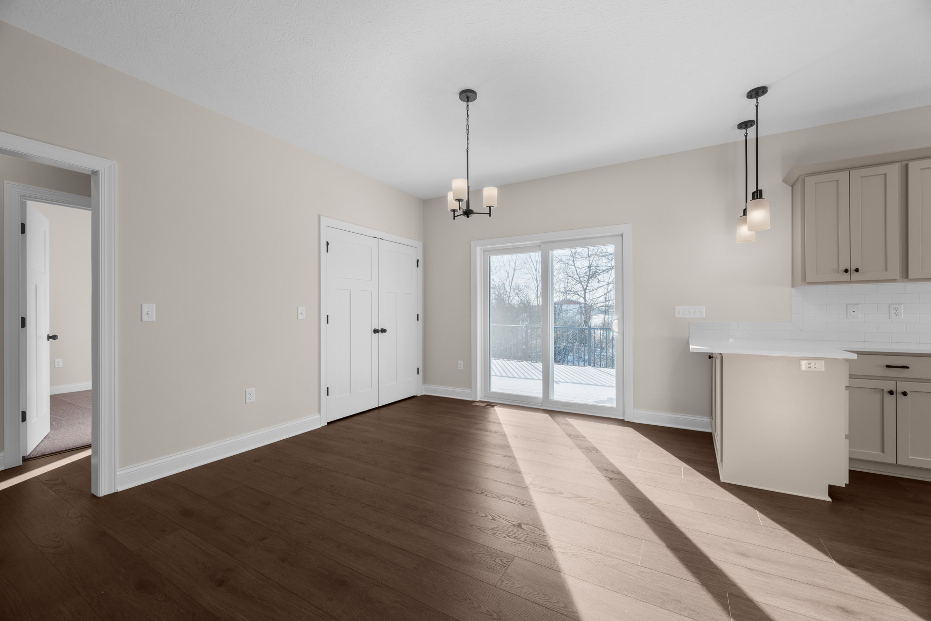 Wood flooring in a bright room with a white countertop, white doors with black knobs, sliding glass door opening to a snowy yard, and a long black pole with a chain.