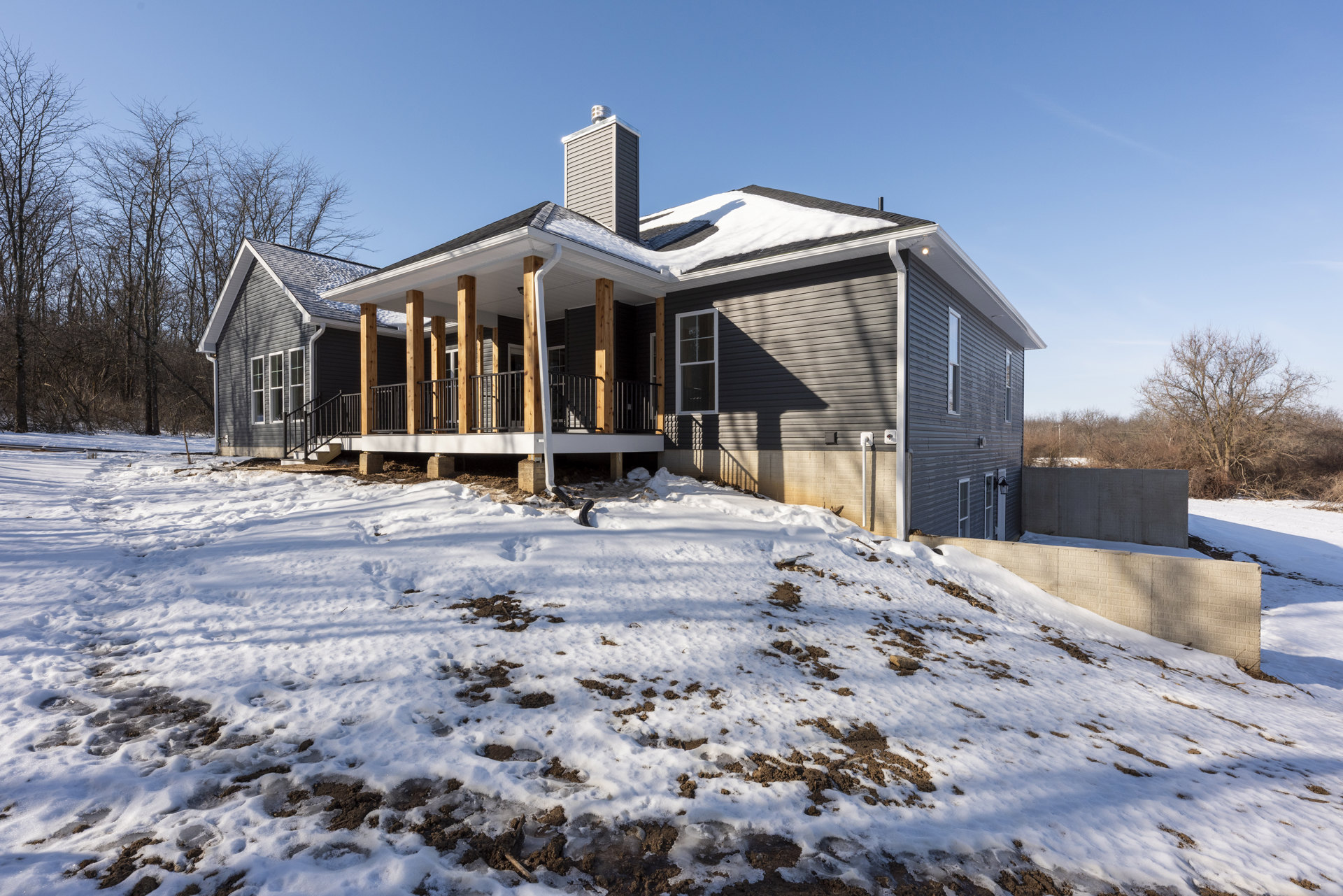 Two-story house with white-framed windows, snow covering the roof and ground, leafless trees in the yard, winter sky overhead