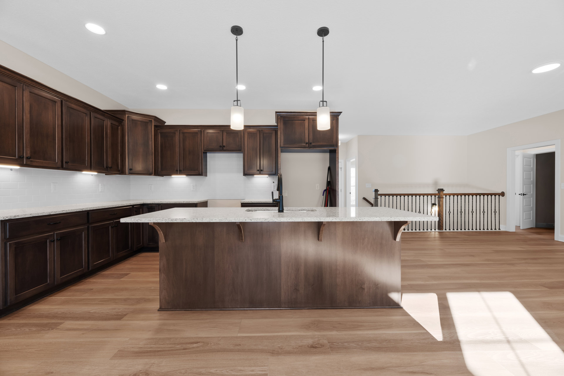 Spacious kitchen featuring a large central island with white countertop, black faucet sink, light wood cabinetry, pendant lights above the island, and light hardwood flooring.