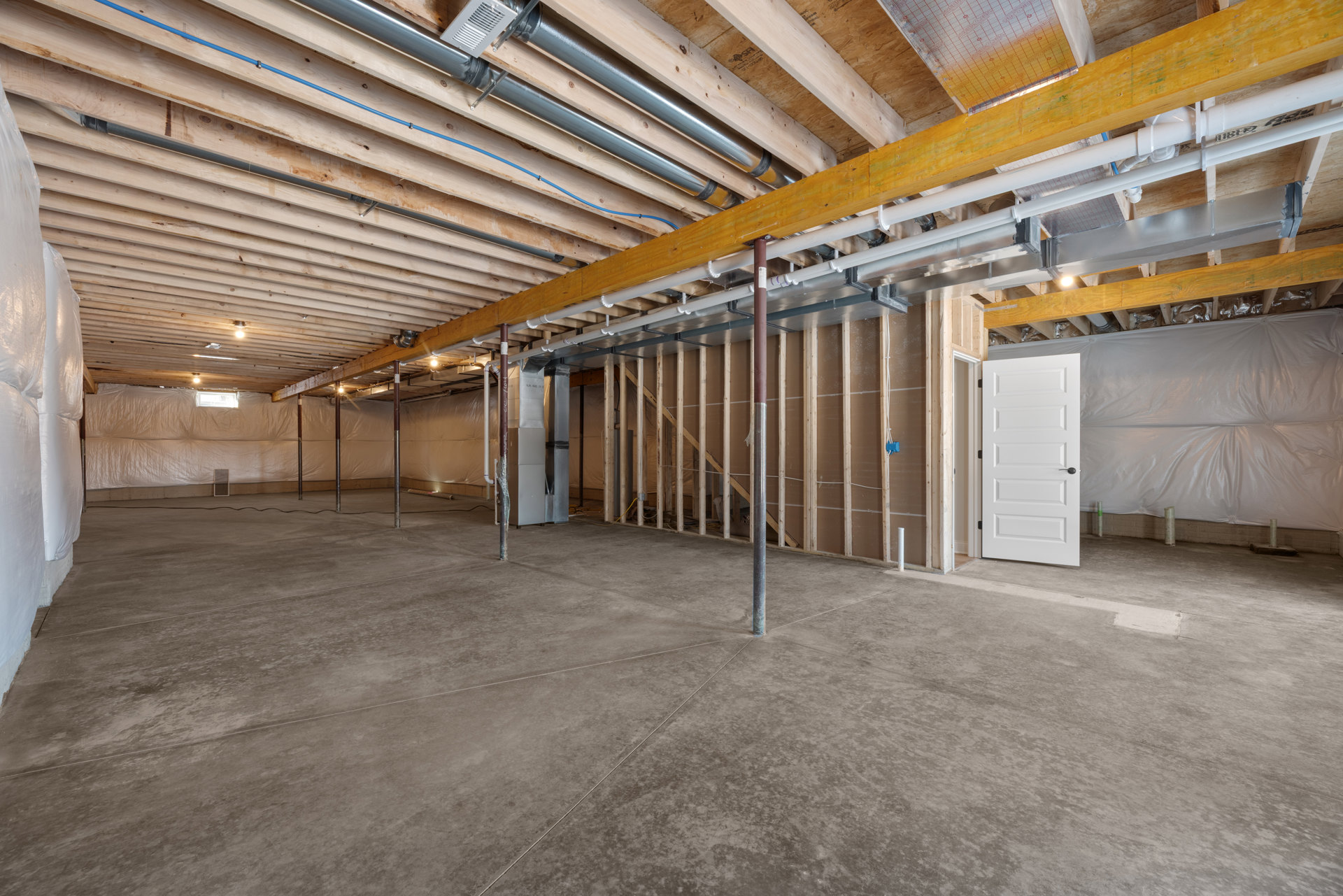 Concrete floor with exposed metal beams and pipes, wooden ceiling, white door with black handle, neutral walls, industrial-style interior