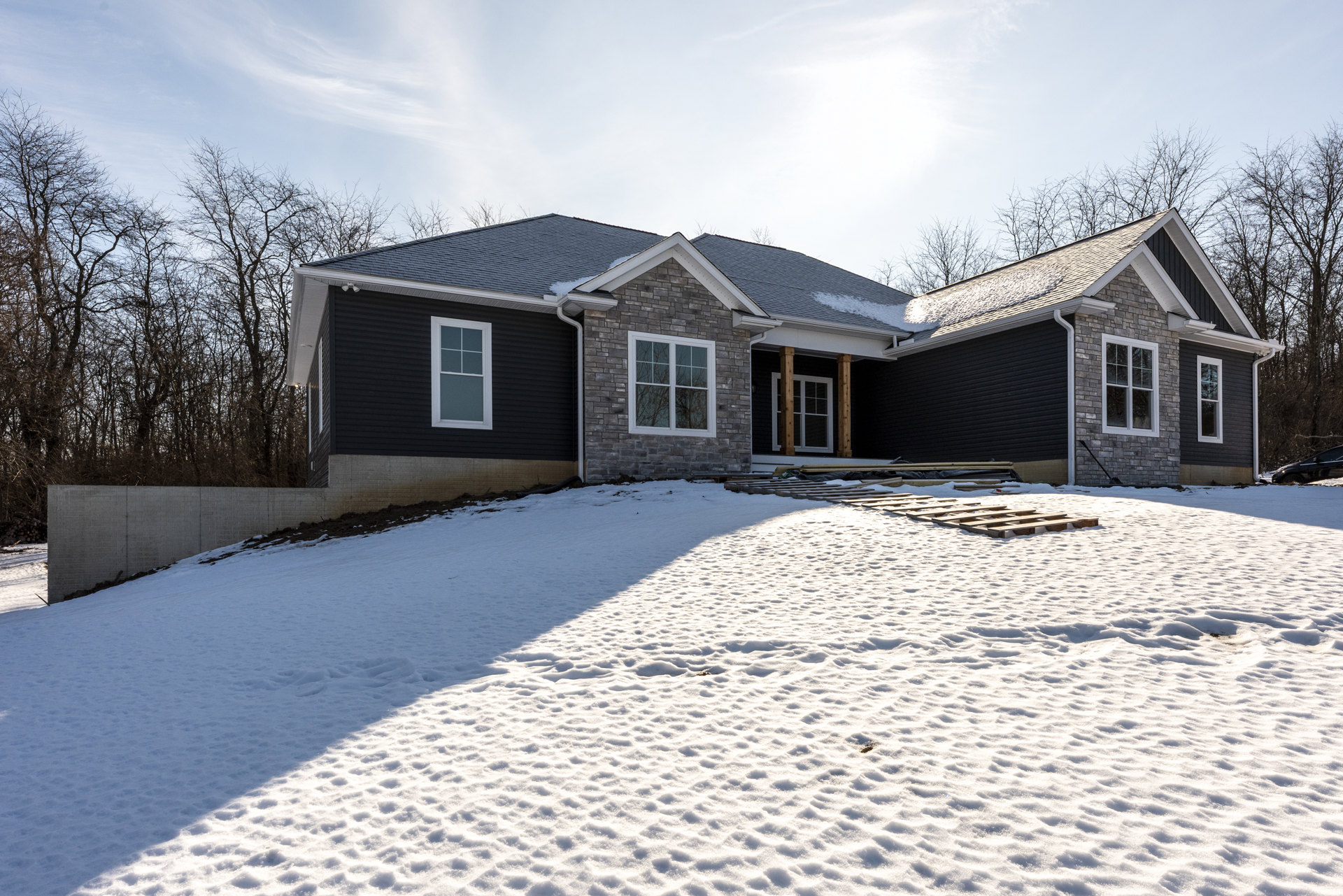 Two-story house with white-framed windows, snow covering the ground and roof, bare trees in the yard, cloudy winter sky overhead