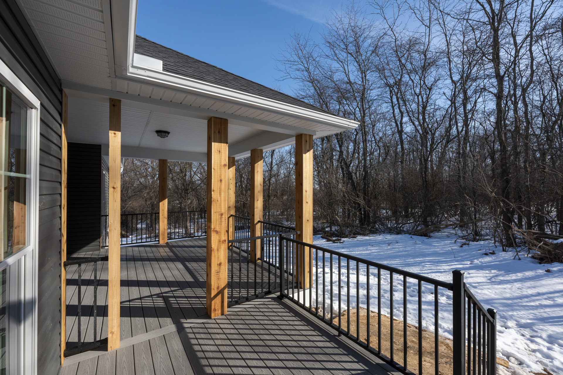 Wood deck with black metal railing overlooking snow-covered yard, wooden fence, and trees in winter