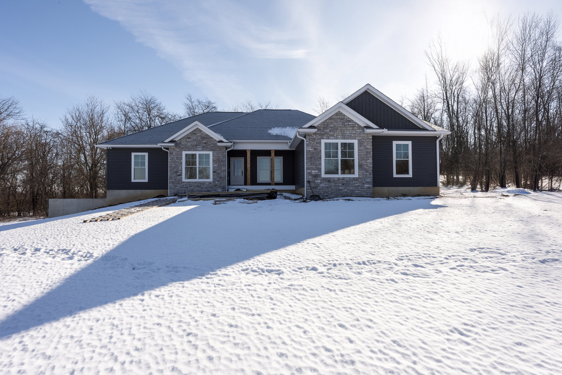 Red brick exterior with white-framed window, snow covering roof and ground, bare trees in winter landscape