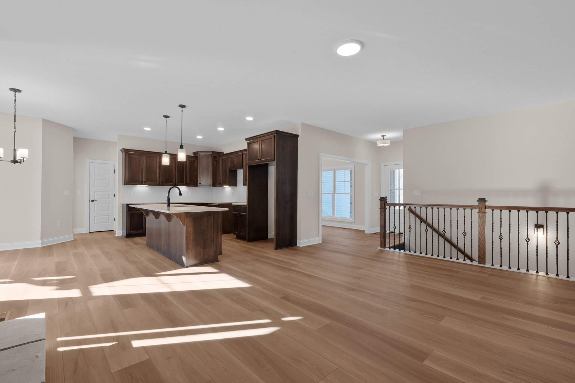 Open-concept kitchen and living room with hardwood floors, marble-topped kitchen island, black faucet, white door with black handle, modern ceiling light, and close-up of wood
