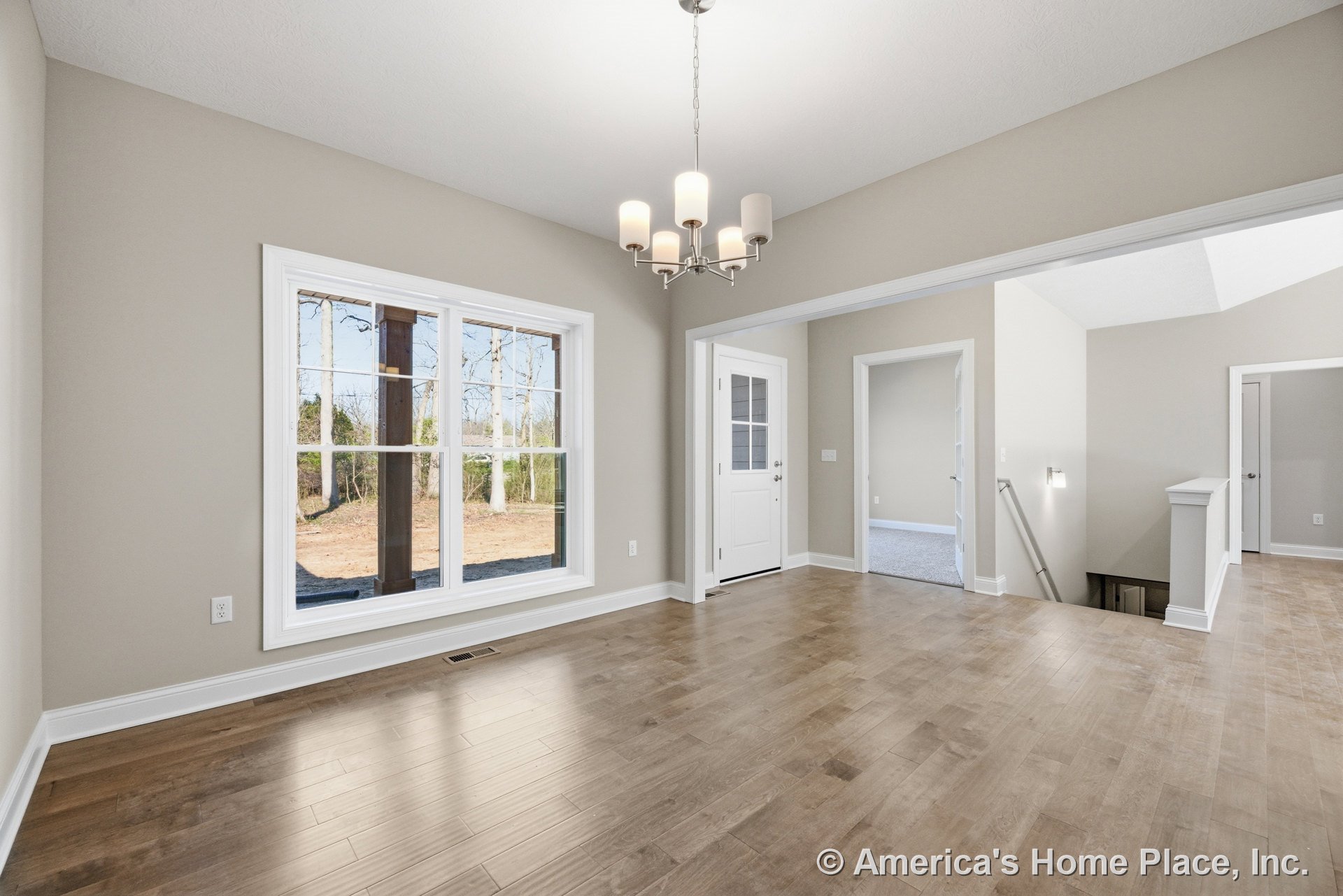 Wide plank wood flooring in foyer with large double-pane window, modern chandelier lighting, white trim and baseboards, neutral wall paint, open stairwell with railing, interior