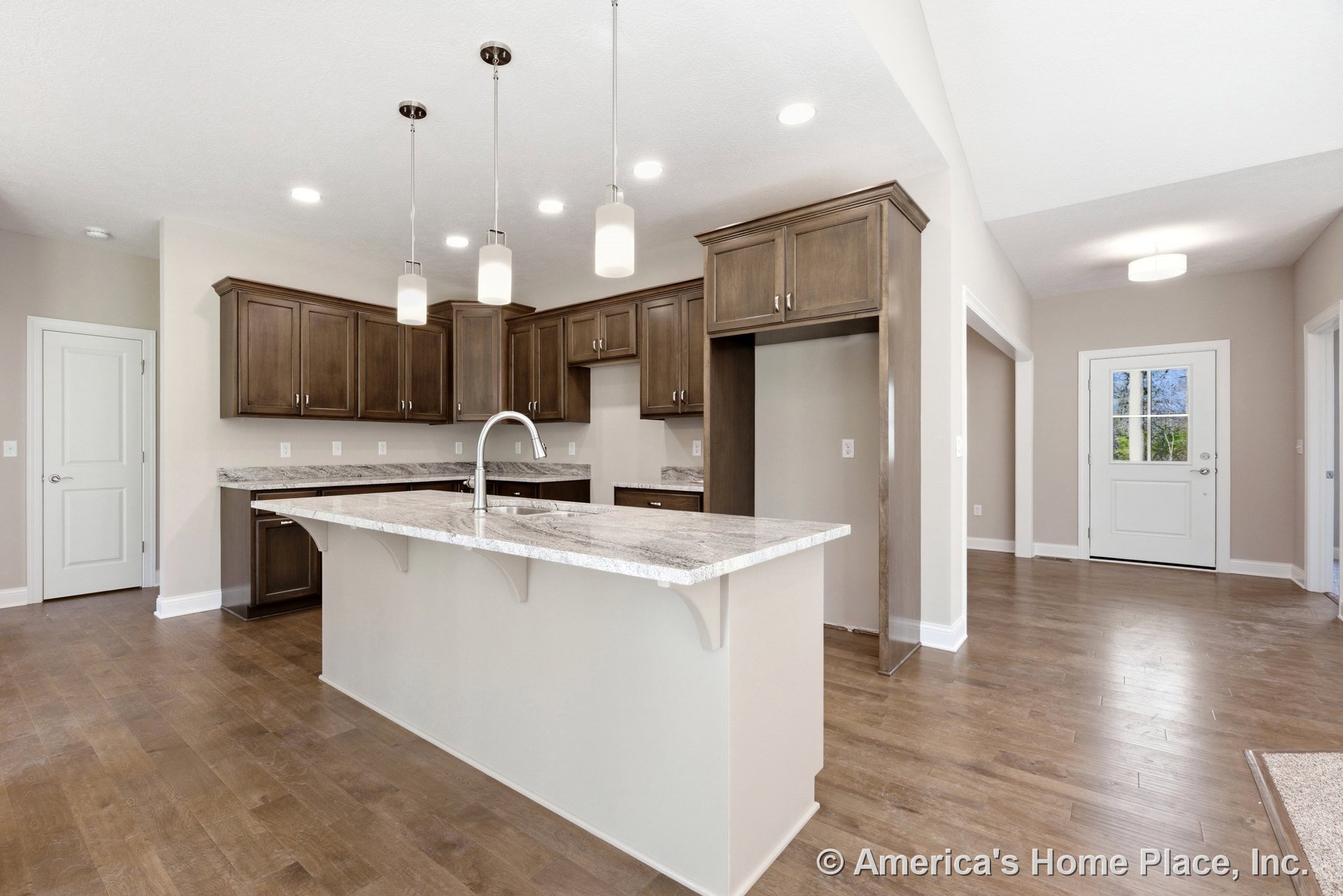 Wood cabinetry kitchen with granite countertops, central island beneath pendant lights, hardwood flooring, recessed ceiling lighting, neutral walls, and open layout with entry door