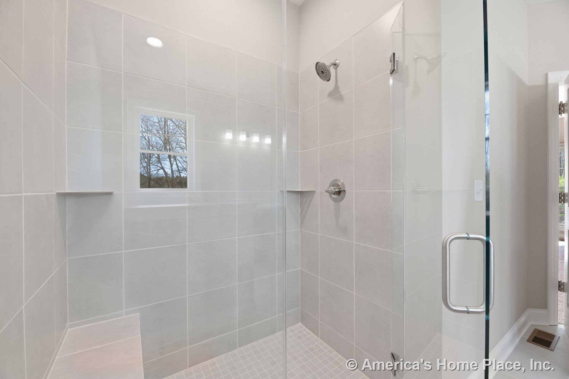 Walk-in shower with large light gray wall tiles, built-in bench, glass enclosure, chrome fixtures, recessed ceiling light, window, and built-in niche.