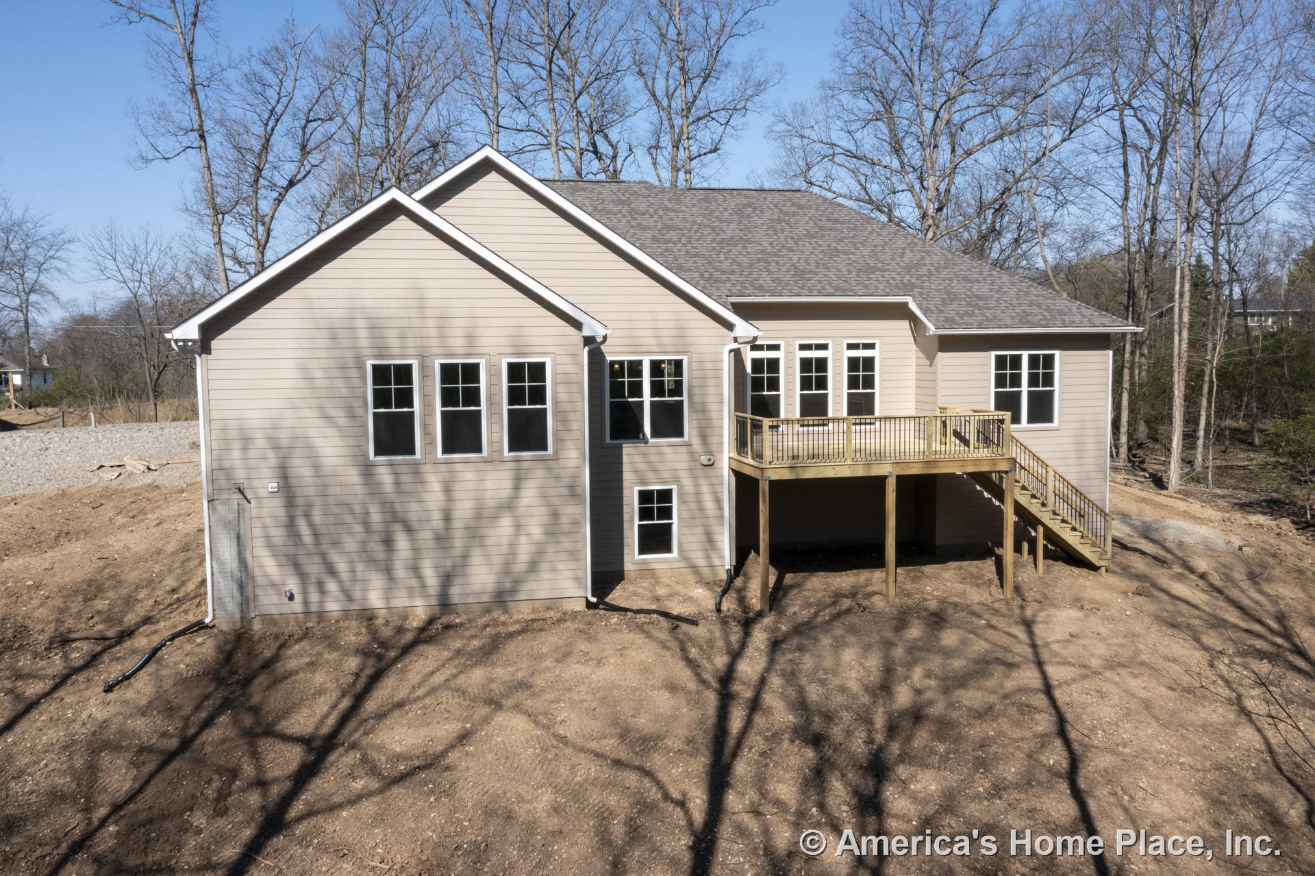 Beige horizontal siding with white trim, multiple double-hung windows, gabled roof, raised wooden deck featuring stairs leading to the yard