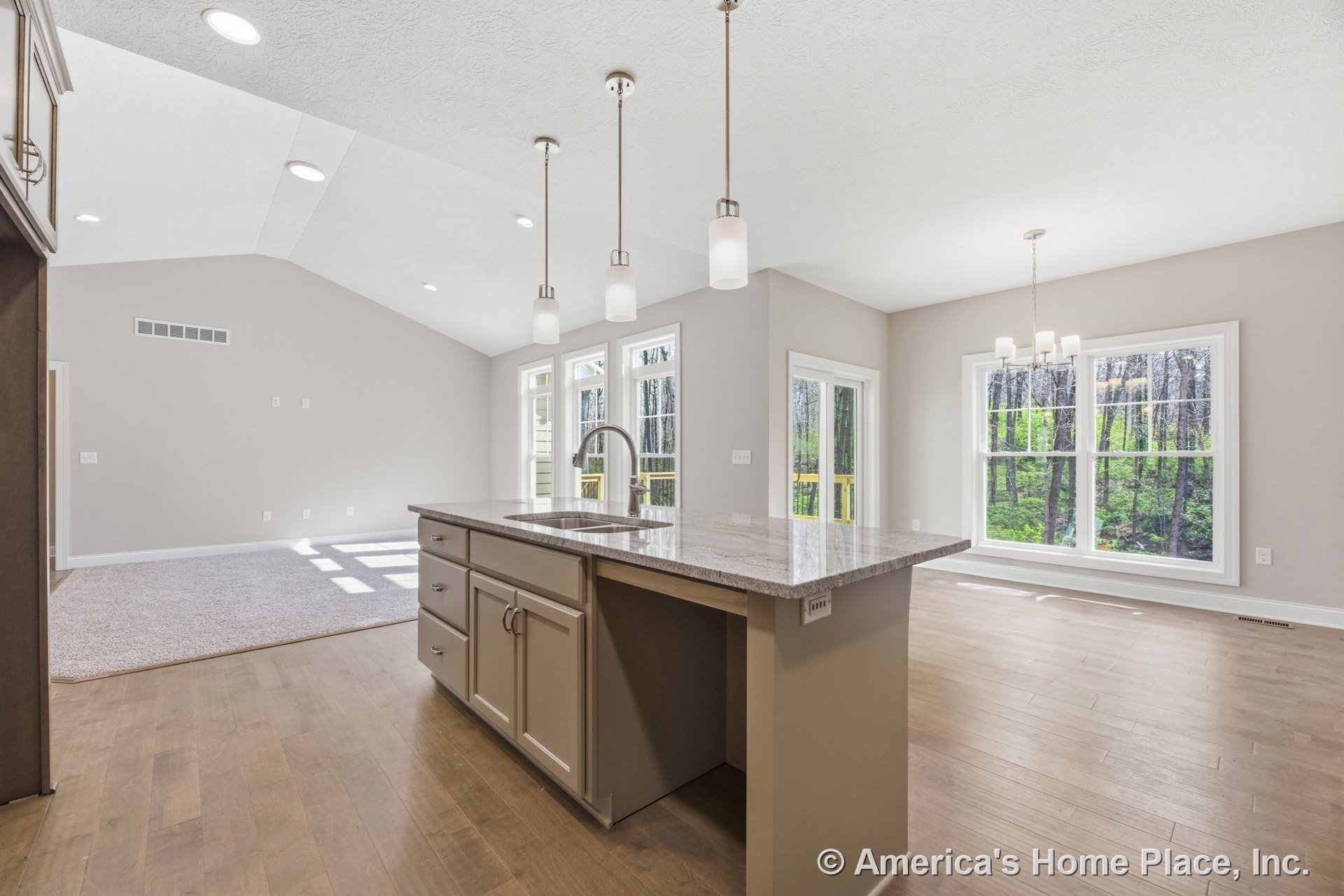 Granite kitchen island with built-in cabinetry and pendant lighting, wide plank wood flooring, open dining area with large double windows, vaulted ceiling featuring recessed