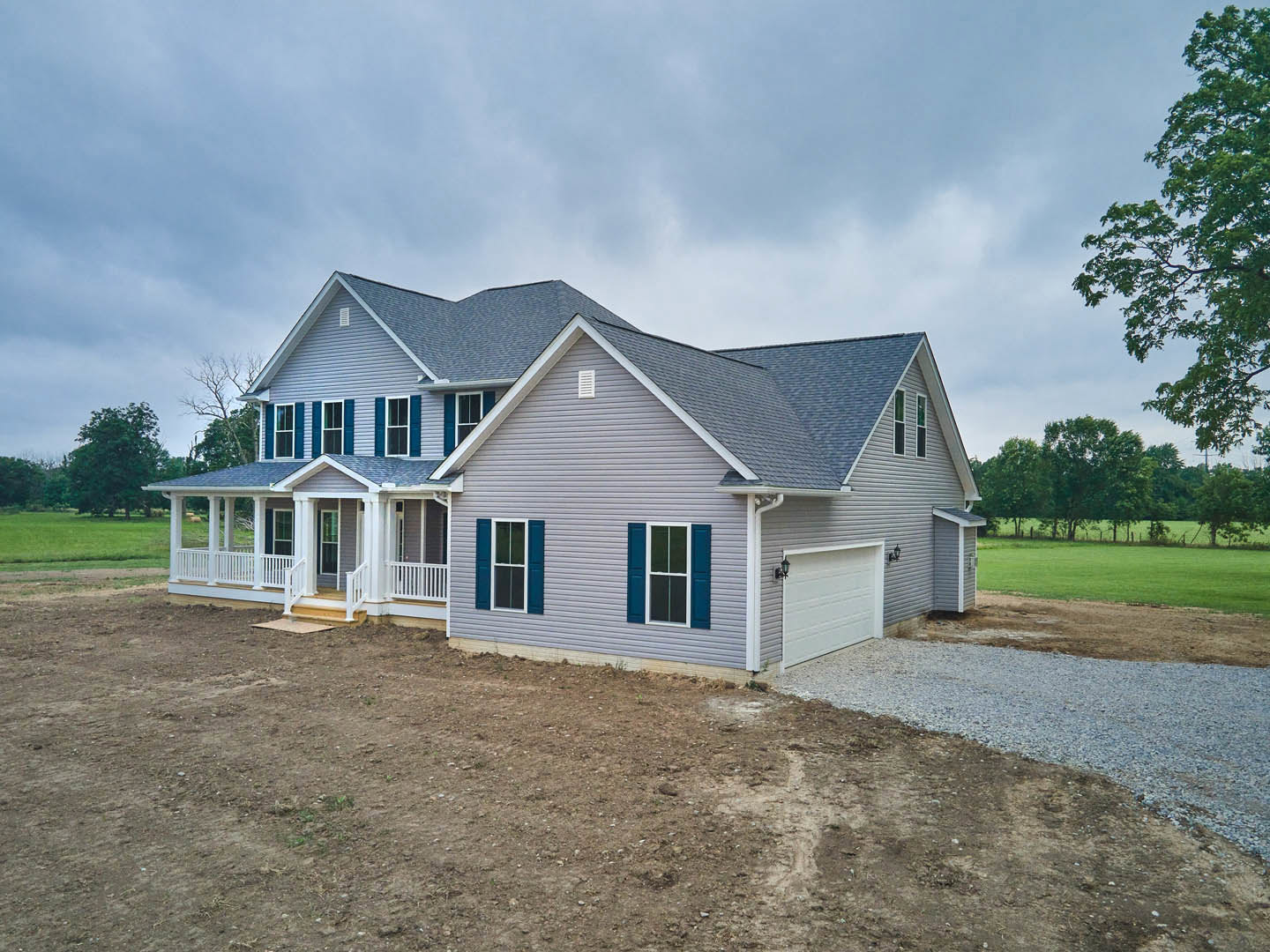 Two-story home with blue roof, blue shuttered windows, attached garage, paved driveway, manicured lawn, and leafy tree in front yard
