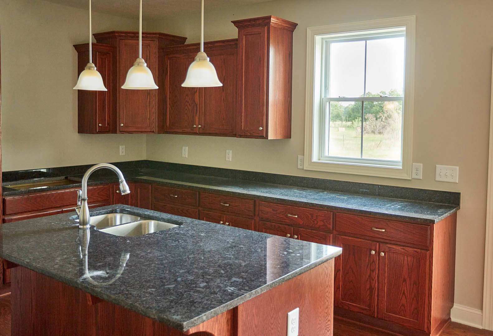 Modern kitchen with white cabinetry, double stainless steel sink set in a stone countertop, large window overlooking a grassy field, close-up of a contemporary light fixture, and a