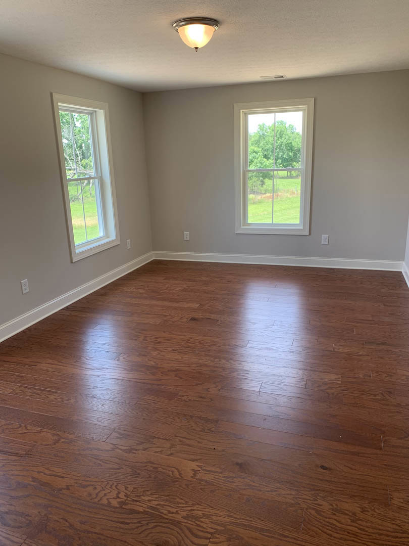 Hardwood floor room with white-framed windows overlooking trees, ceiling light fixture illuminated