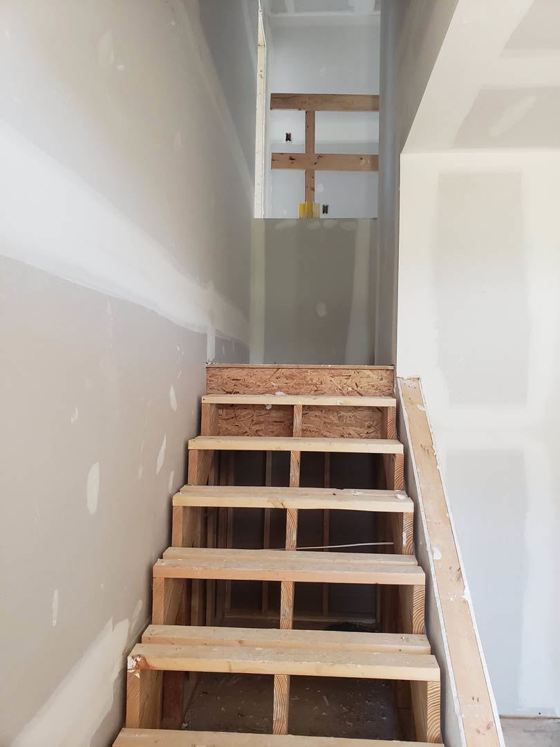 Wooden staircase with natural wood treads and risers, adjacent to a white plaster wall featuring vertical wood plank accents.