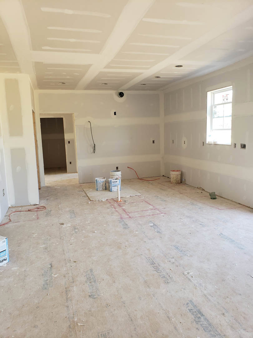 White-walled room with scattered paint cans, white-framed window, red extension cord hanging on wall, unfinished flooring, and square electrical outlet.